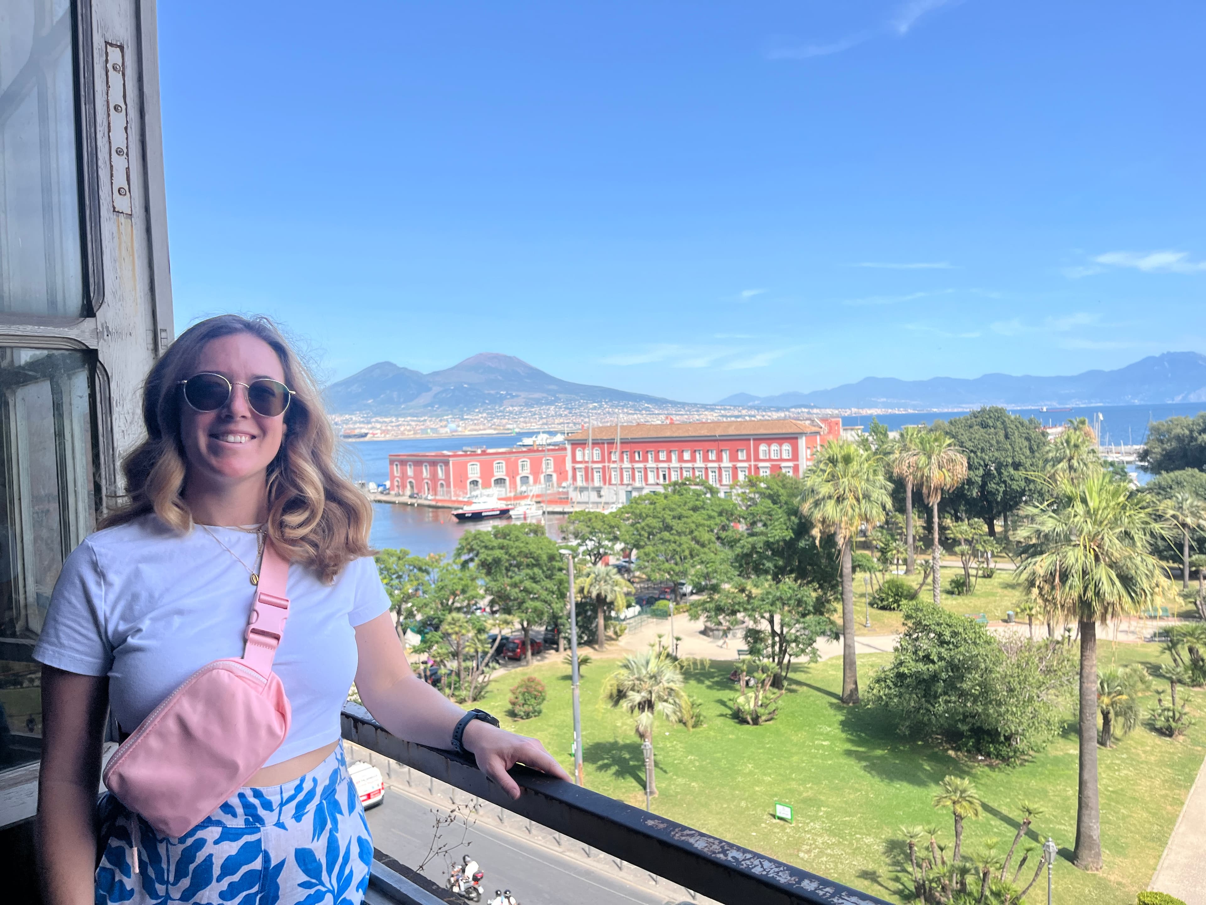 Advisor posing in a large open window overlooking a coastal park with the sea and mountains in the distance
