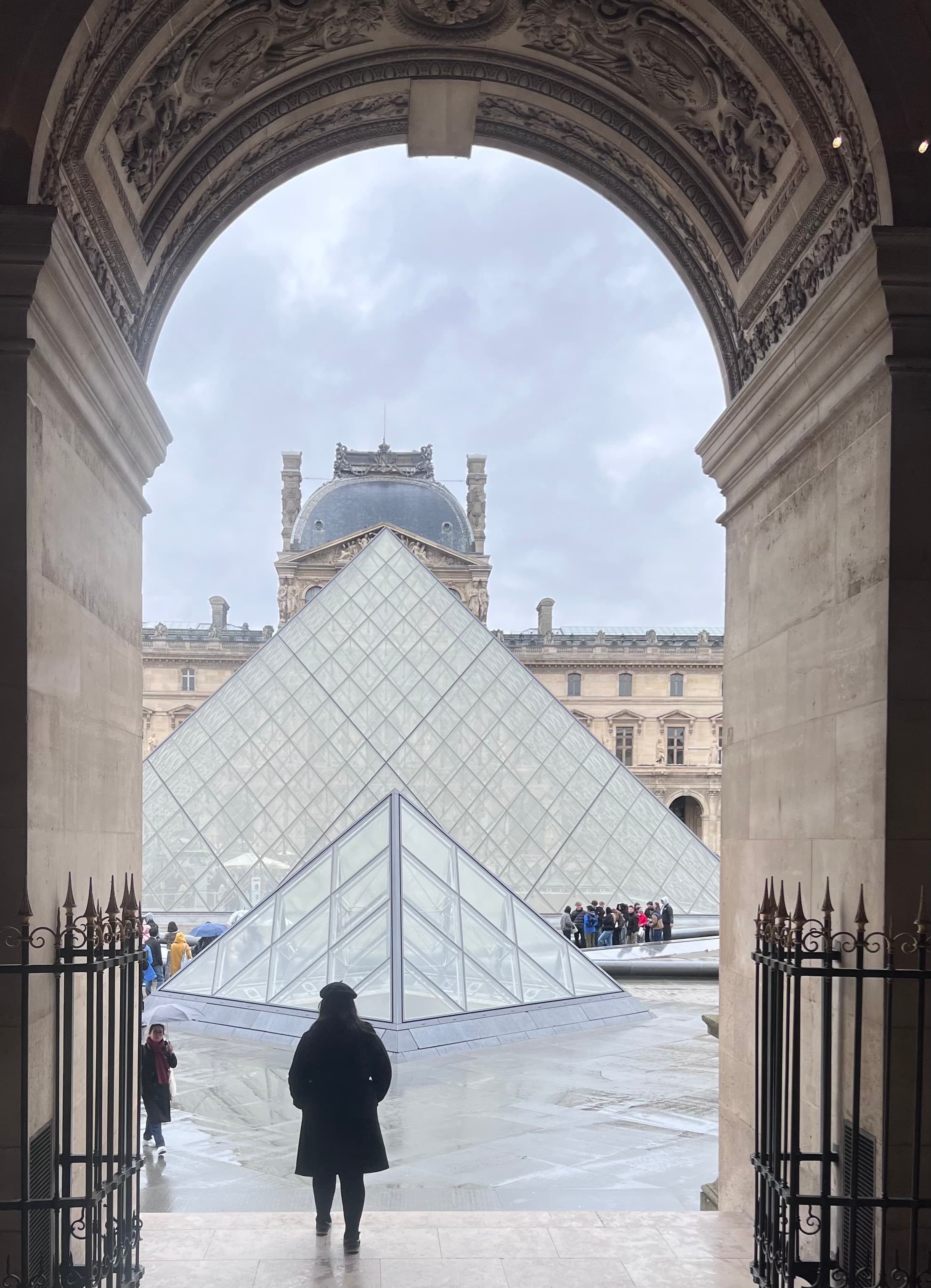 A person silhouetted in a hallway with the glass pyramid of the Louvre ahead of her.
