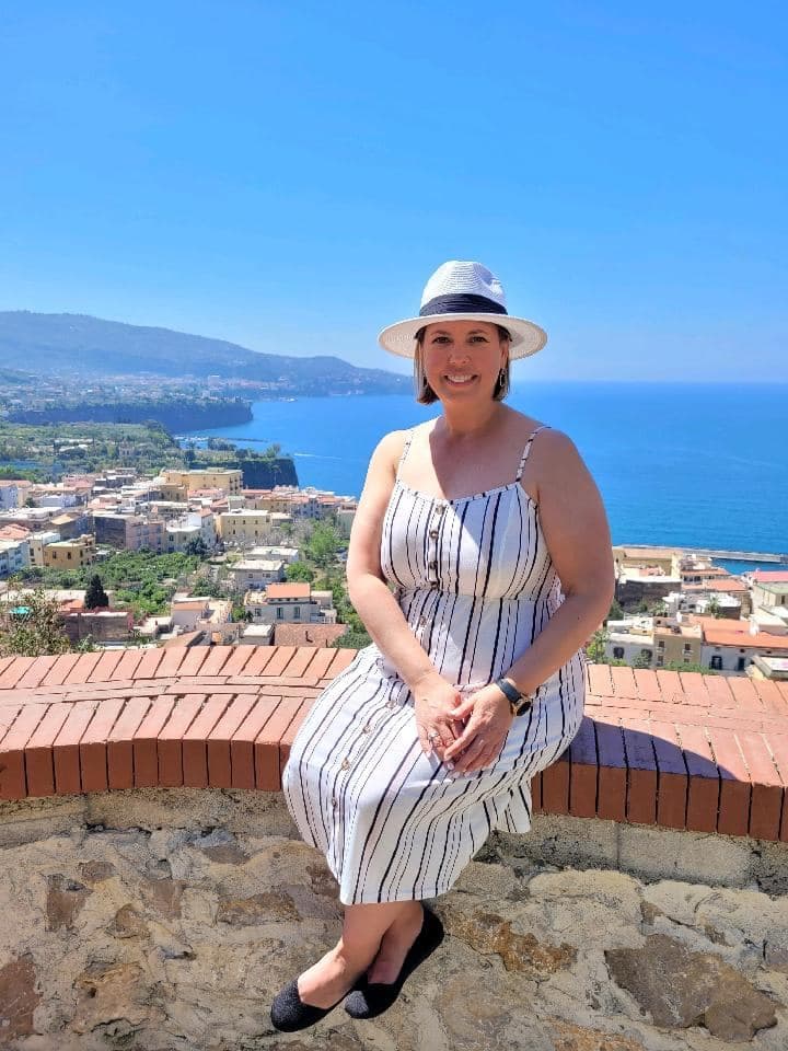 Advisor in a long white striped dress sitting on a ledge overlooking a beautiful coastal city