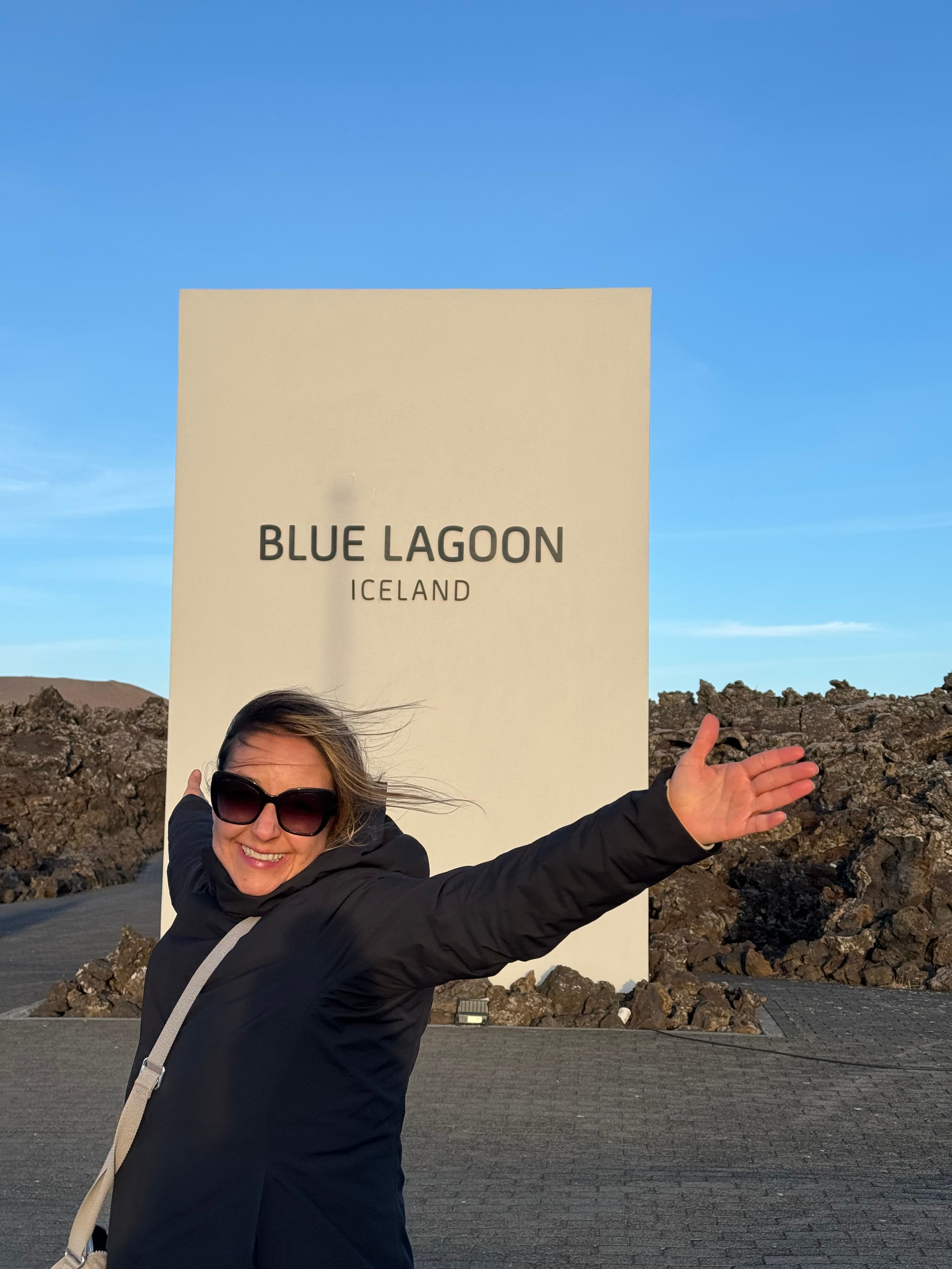 Karla posing with hands in the air in front of a sign that reads "Blue Lagoon Iceland".