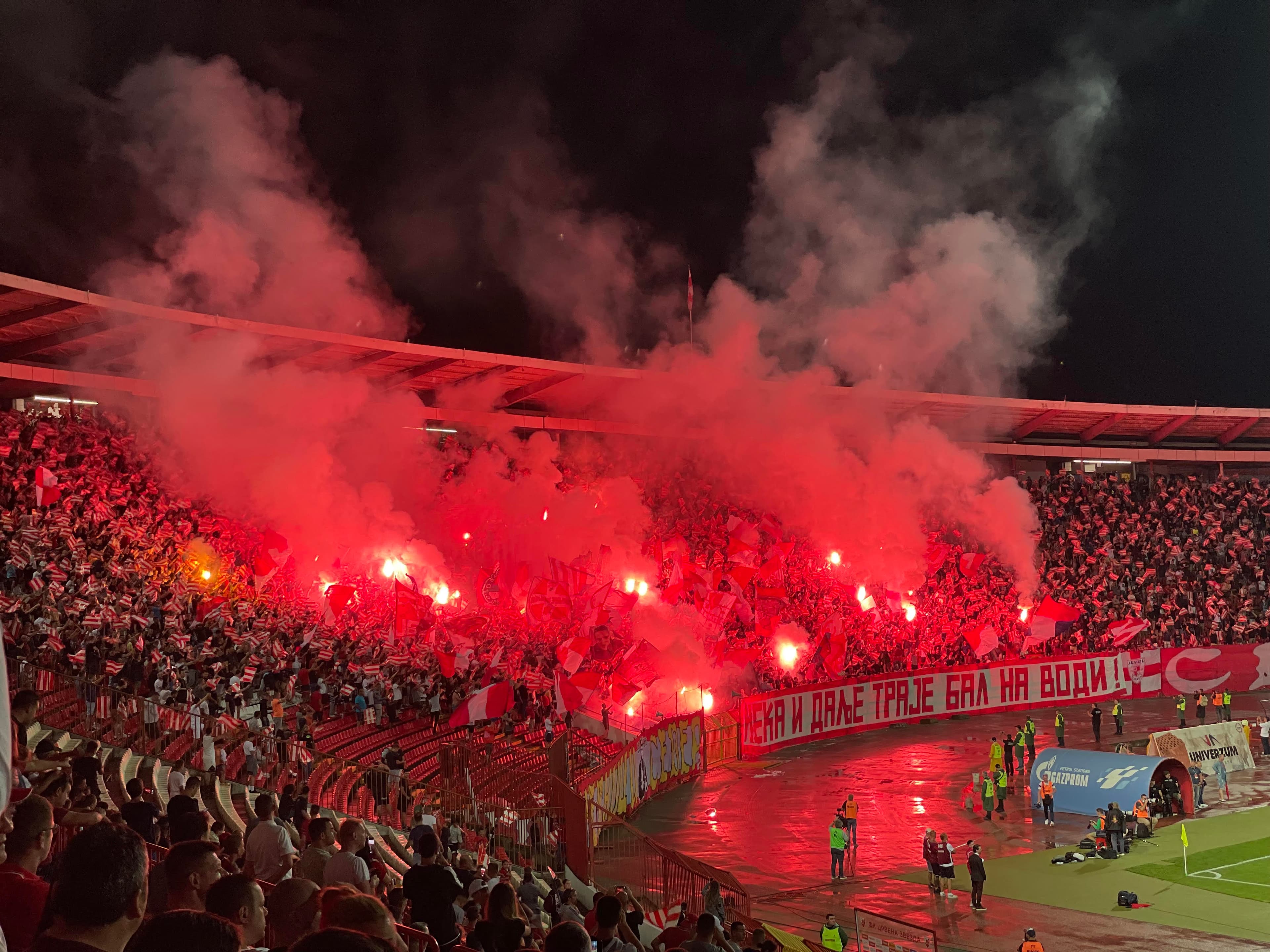 View of red flares lit in a crowd of people in stadium seating at night