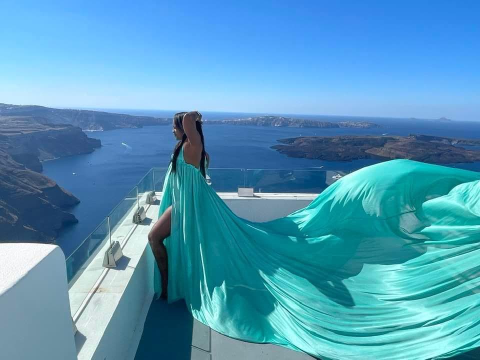 View of advisor in a long flowing turquoise gown standing on a balcony overlooking the sea