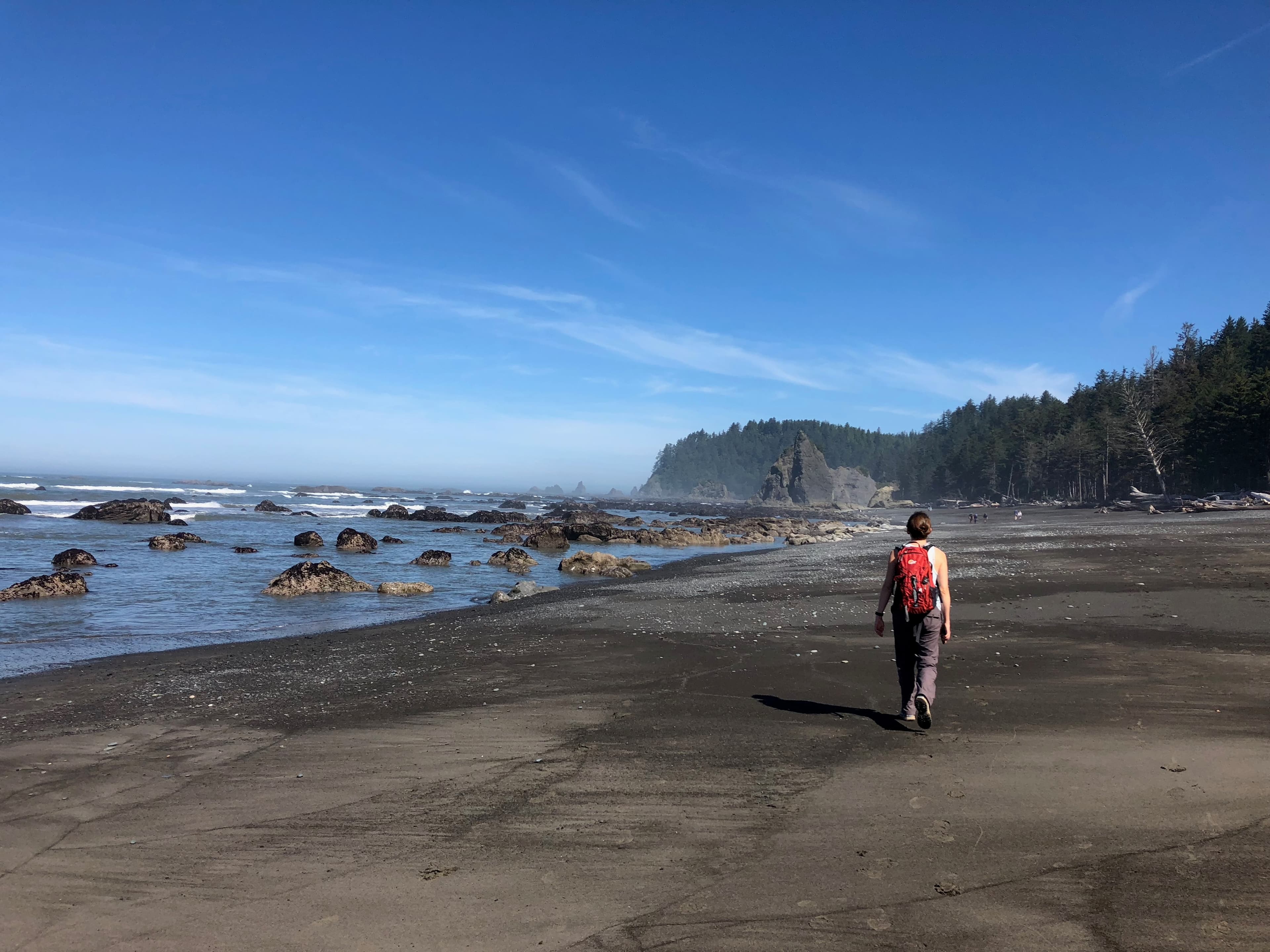 One person walking along a wide empty beach on a sunny day