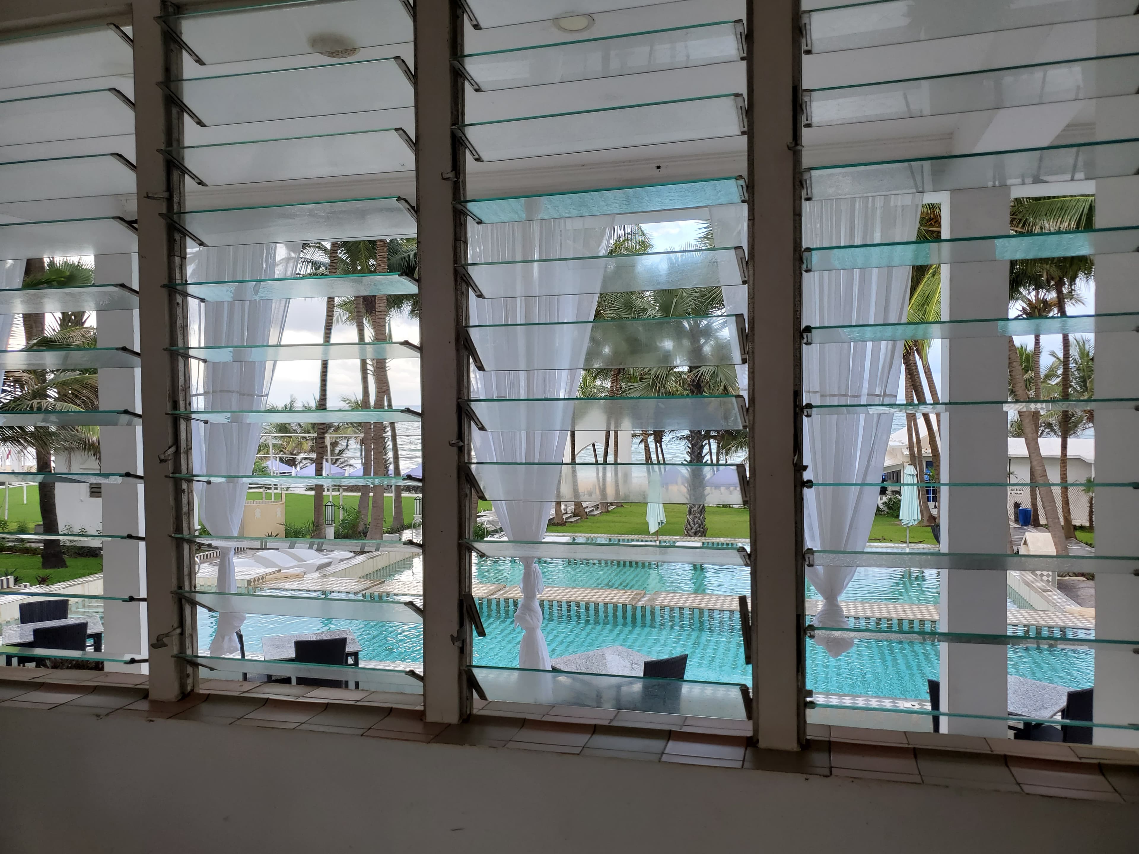 Small hotel pool with hanging white curtains to one side visible and trees in the background