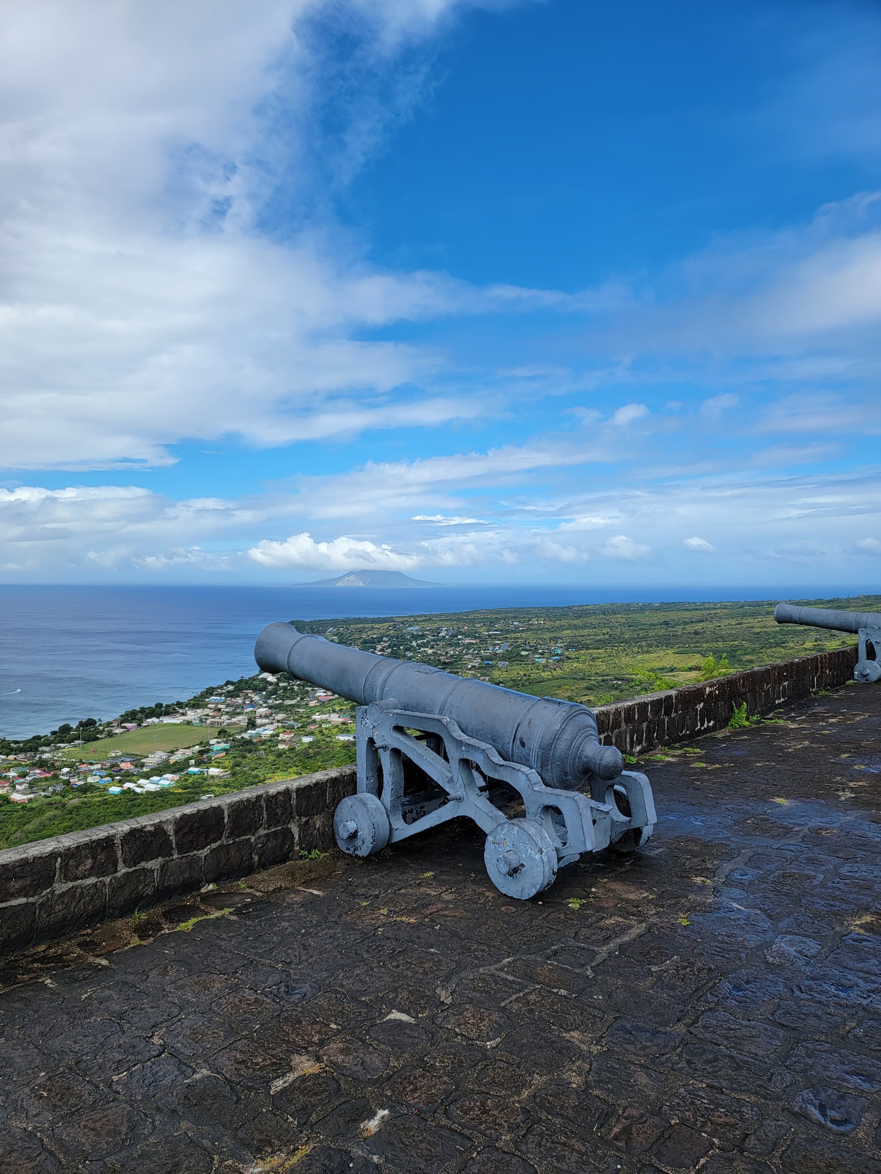 A picture of a grey cannon pointed toward a view of land and sea.