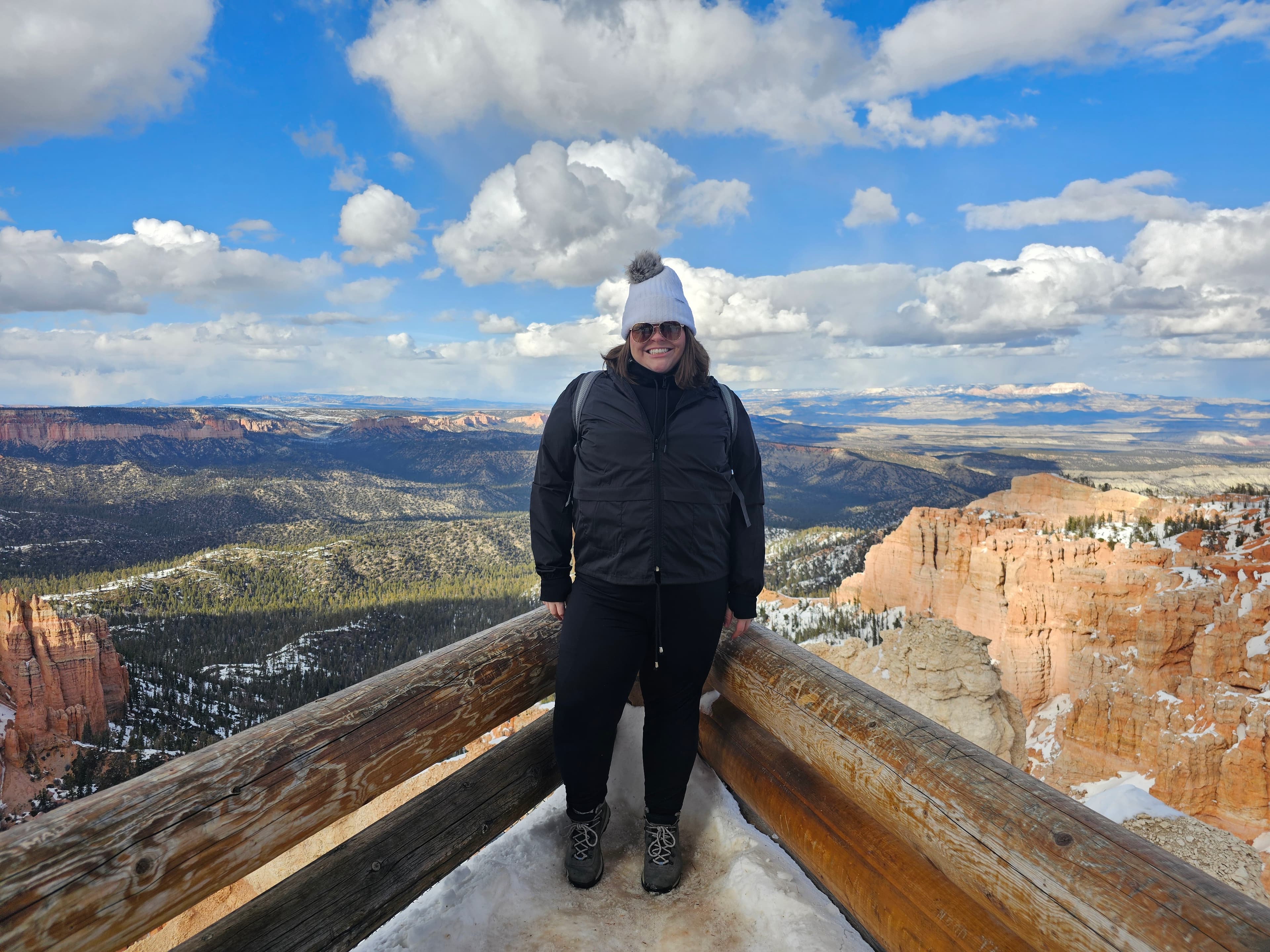 An advisor wearing black outerwear and a grey knit hat, while posing in front of a view of the grand canyon.