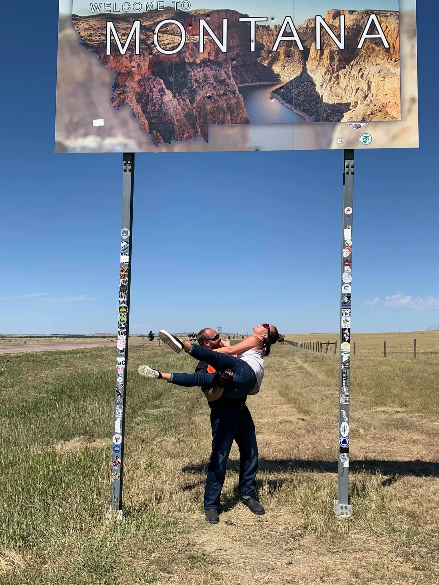 Advisor in the arms of a man under a sign that reads "Montana" during the day.