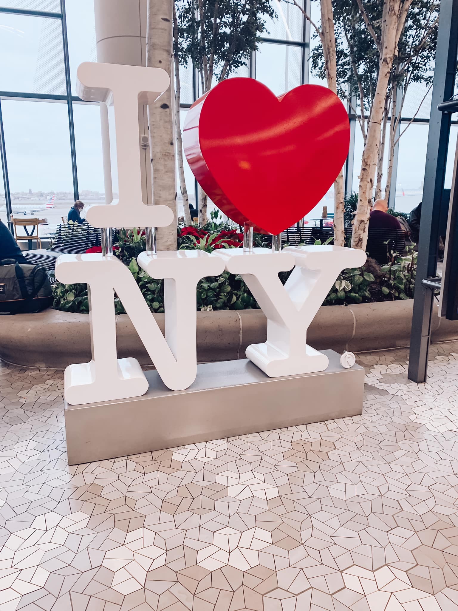 A picture of a large white sign that reads "I heart NY" indoors with windows and plants behind it.