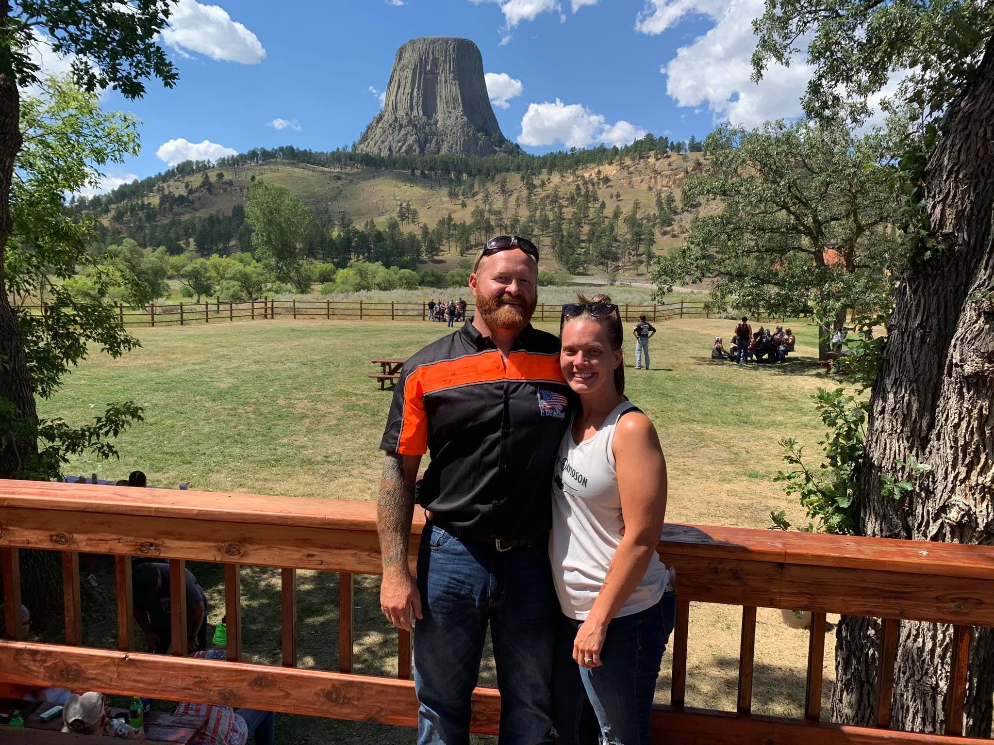 Advisor posing on a deck in front of a grassy valley with a large towering rock formation during the day.
