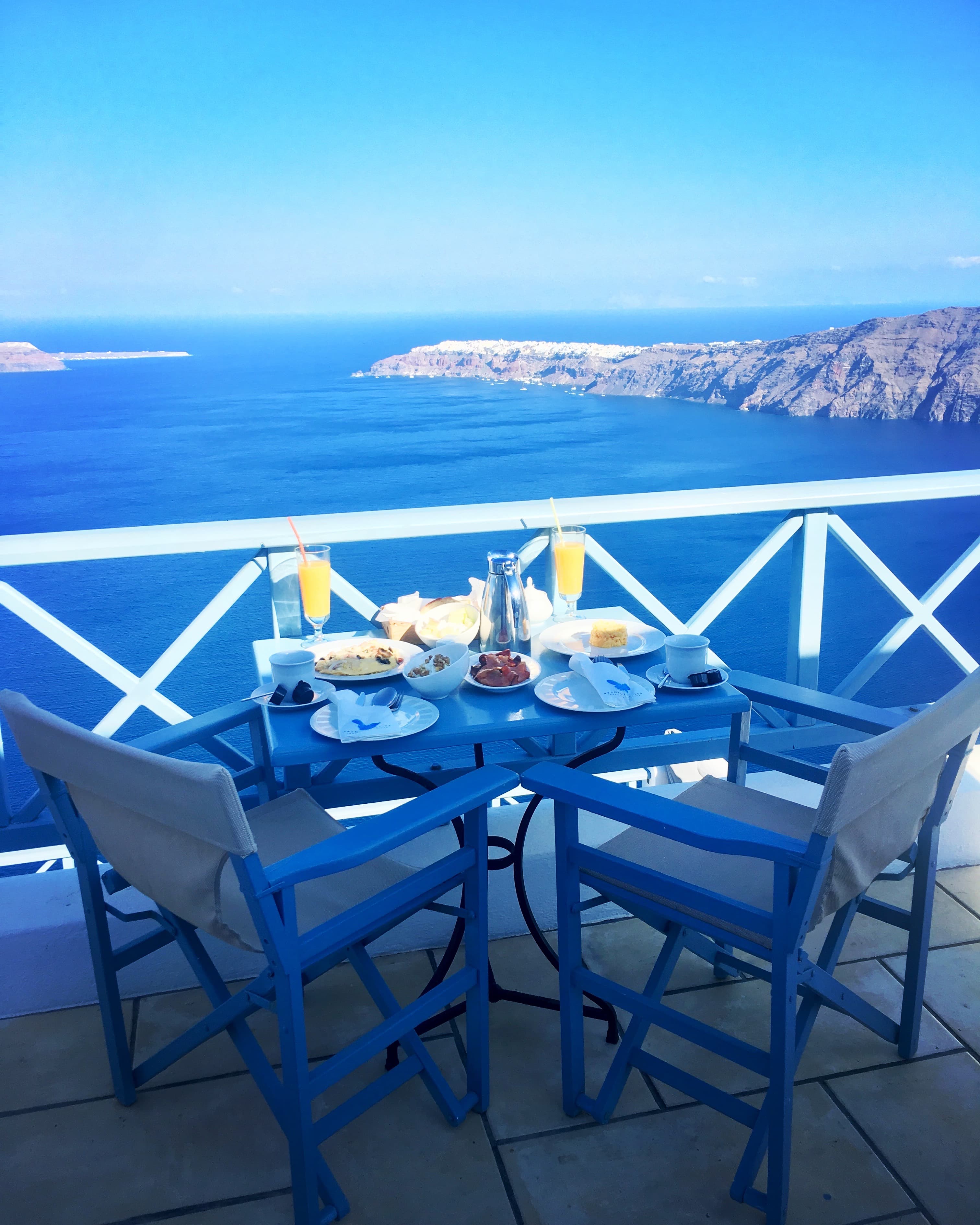 A patio table set for dinner overlooking the ocean on a clear day.
