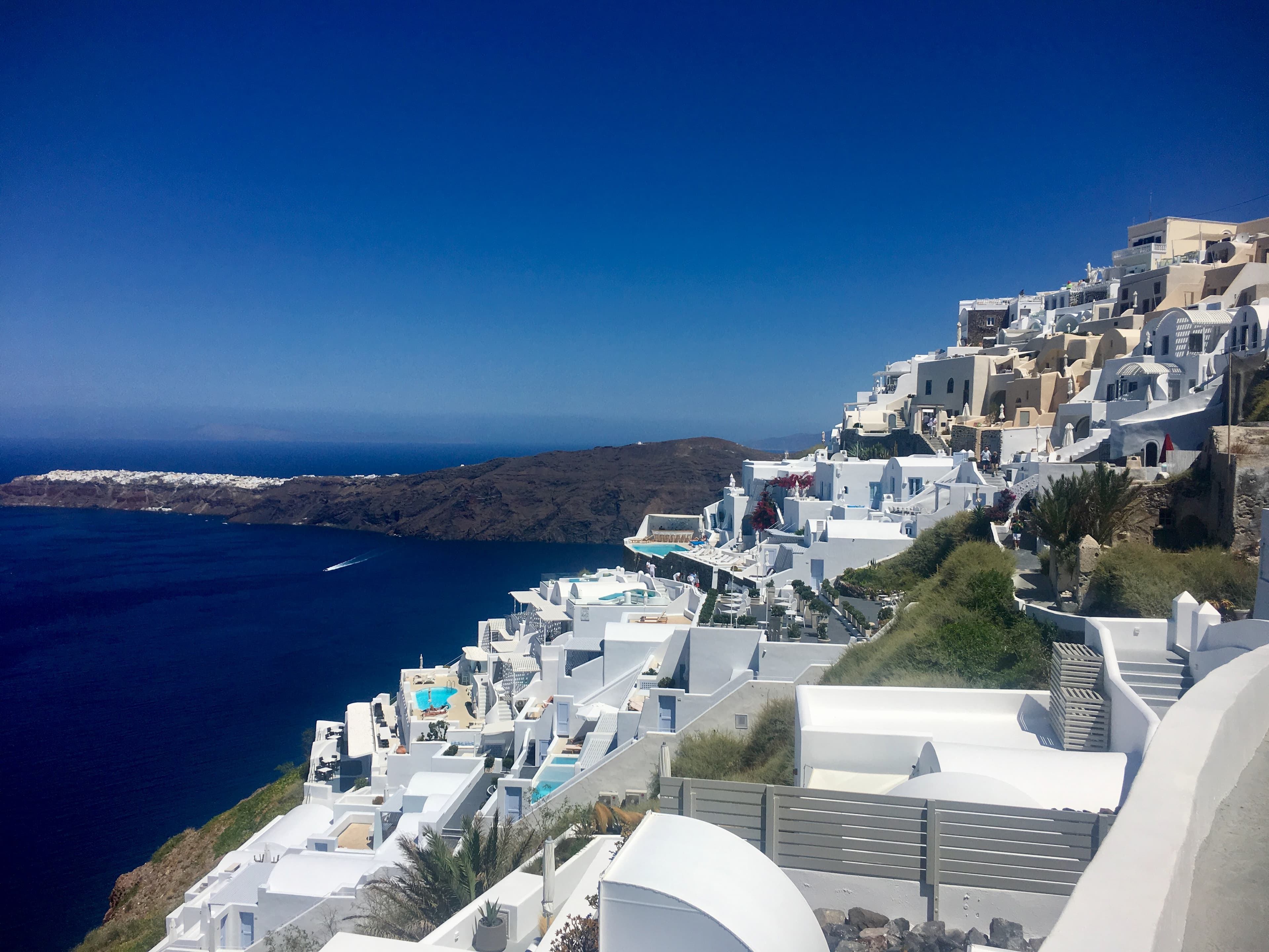 A coastal town built along a hillside as waves lap the shore on a sunny day.