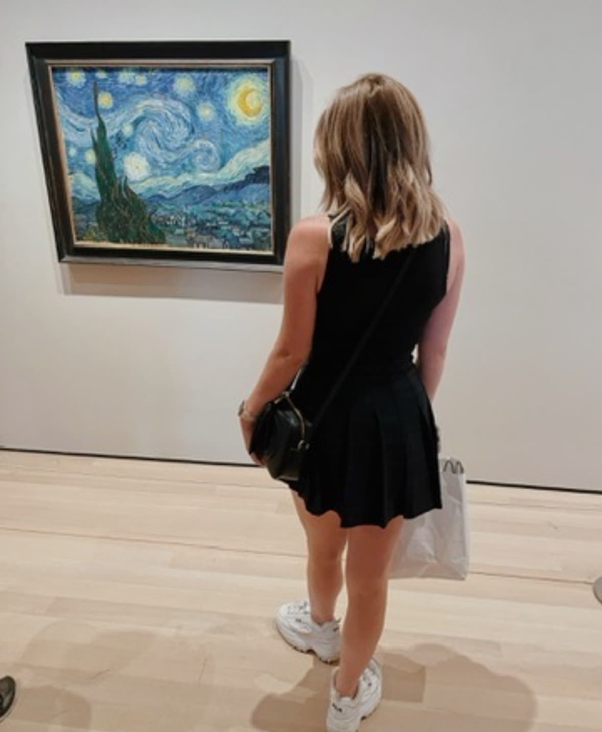 An advisor wearing a black dress and looking at Vincent Van Gogh's Starry Night painting on display at a museum.