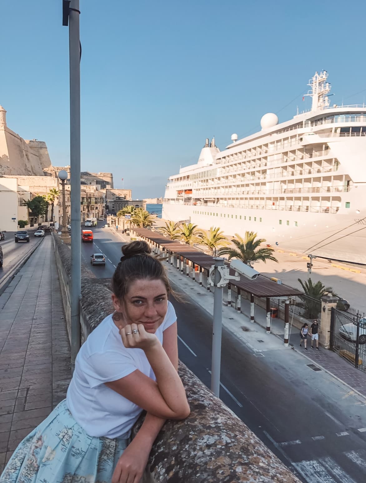 An advisor posing against a stone ledge in front of a view of a large white cruise ship.
