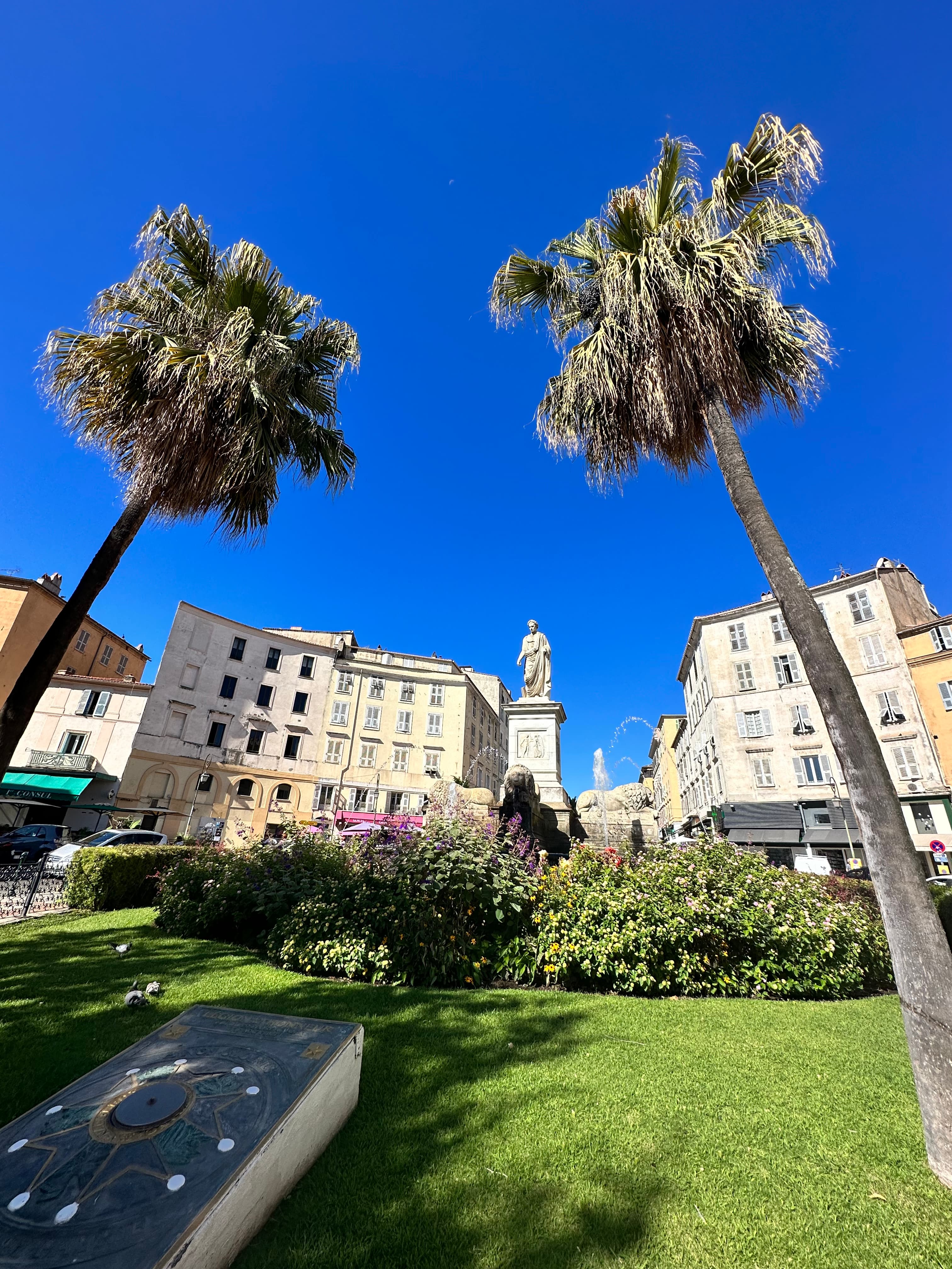 View of two palm trees and a statue in a pretty plaza under clear skies