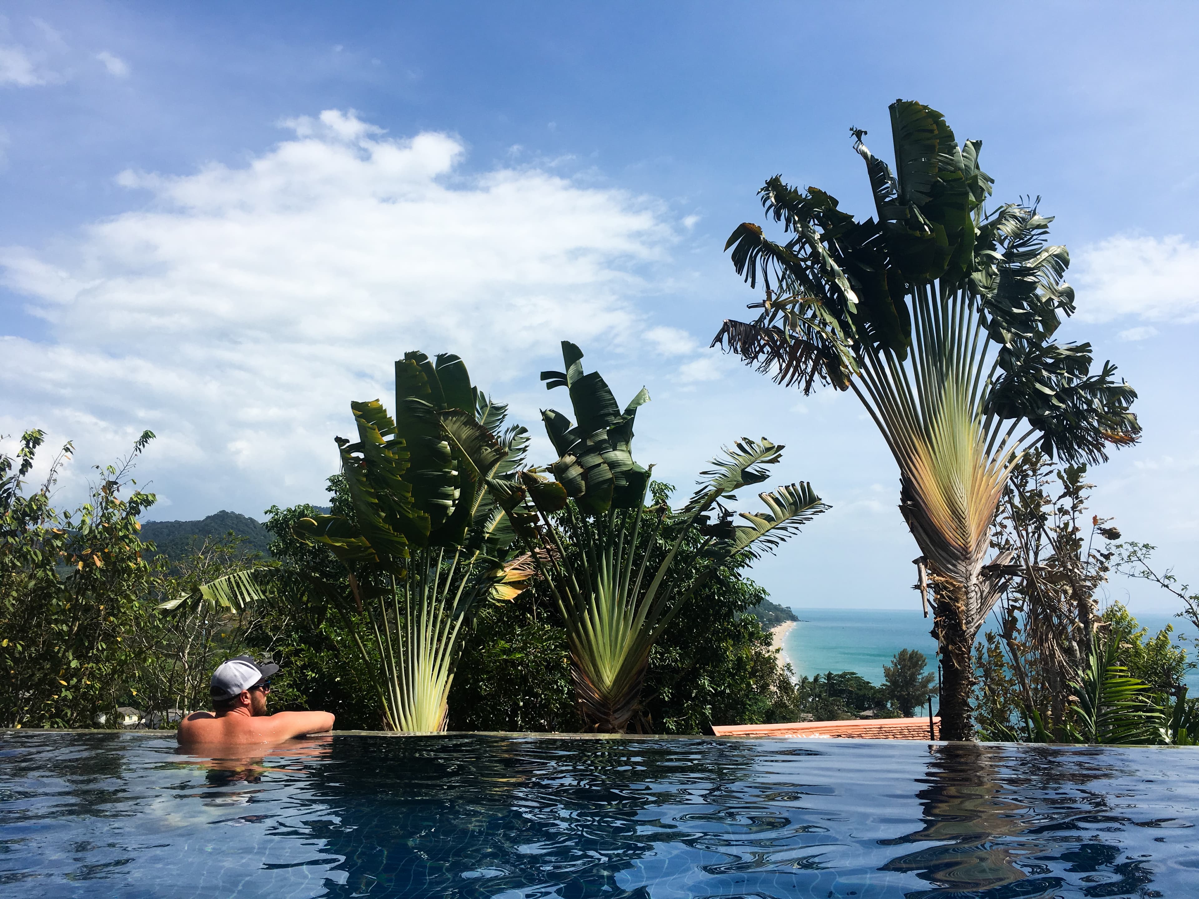 View of a man leaning over the edge of an infinity pool on a sunny day