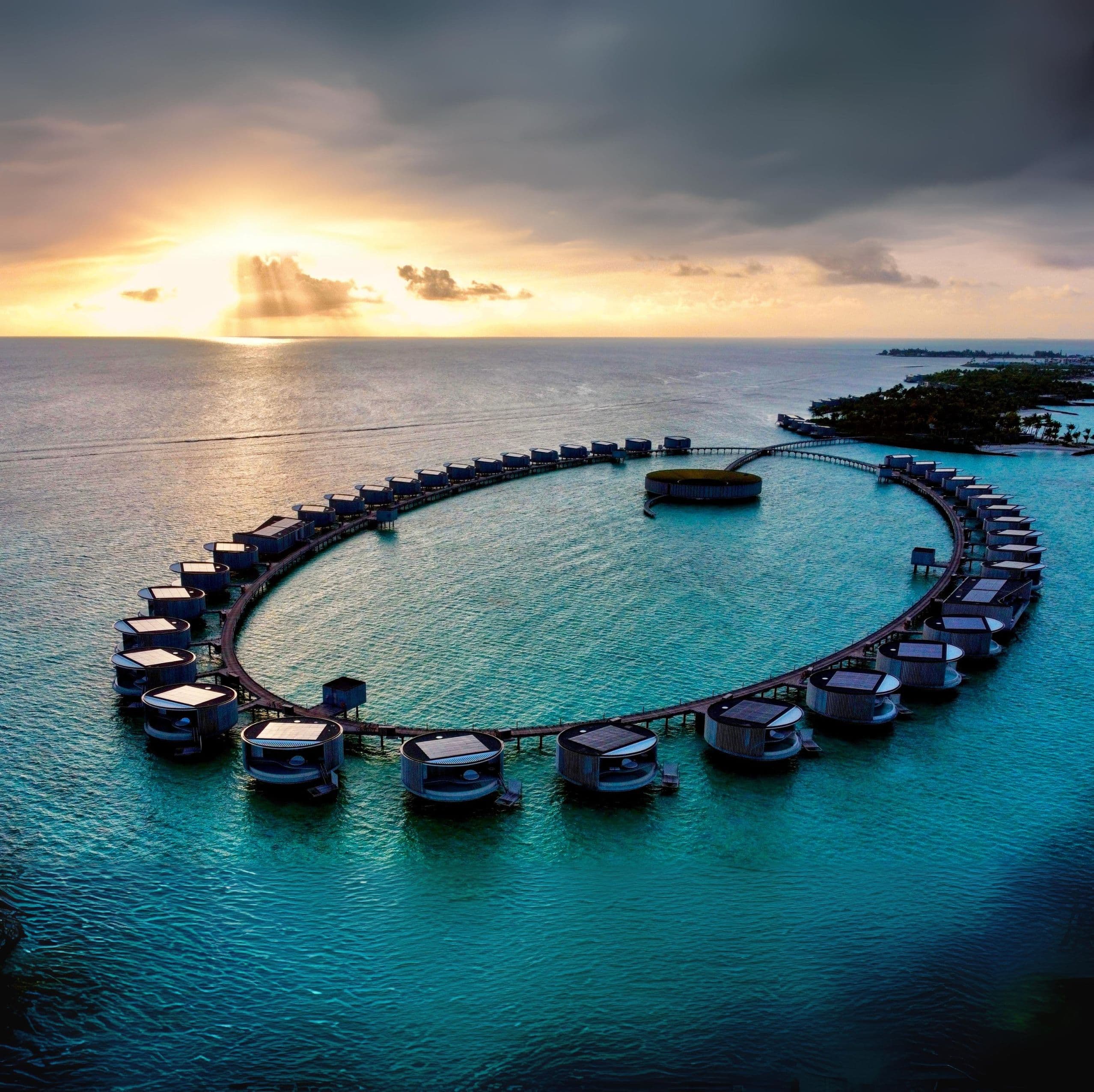 A view of hotels built in the ocean with a sunset in the distance.