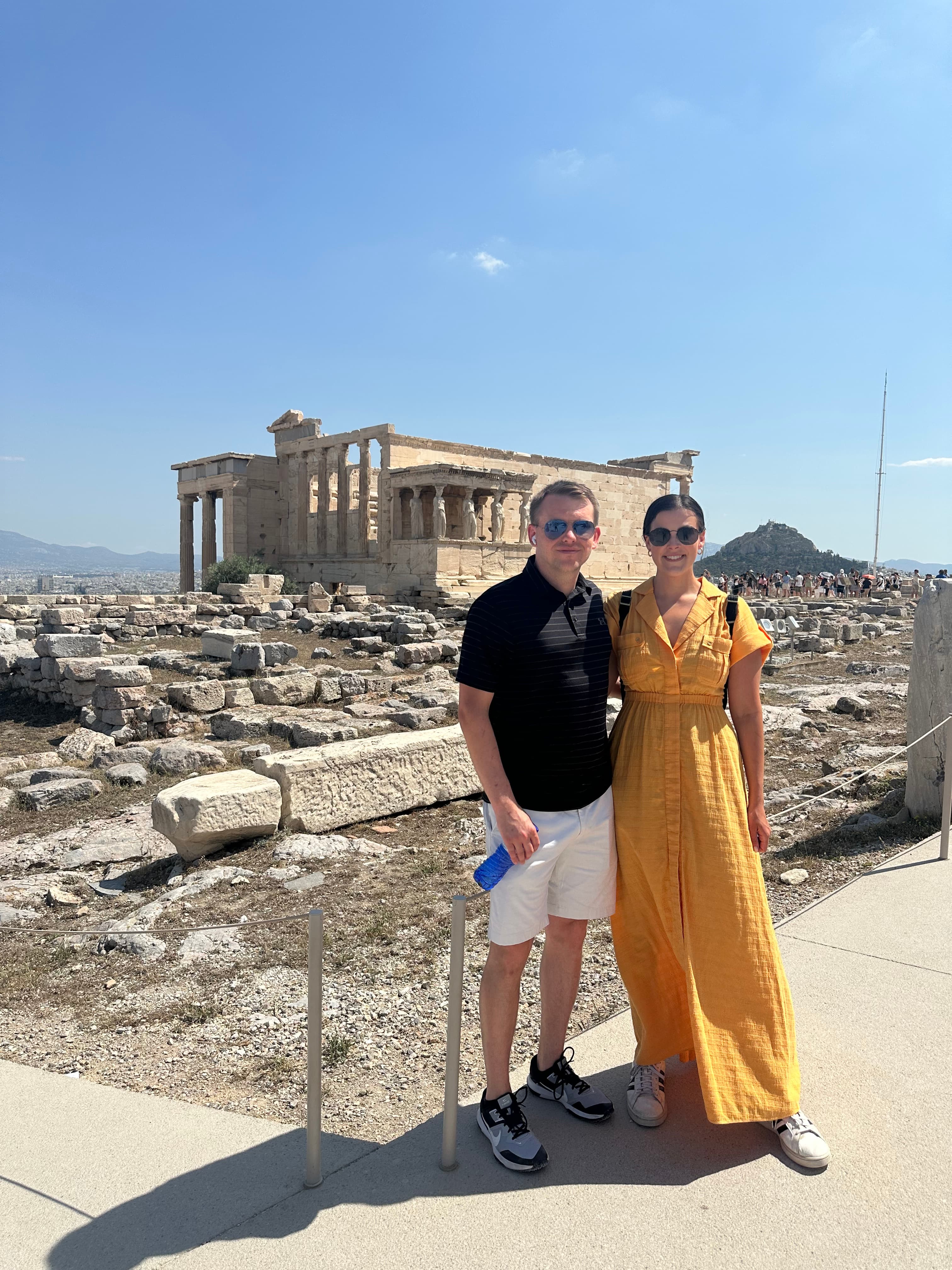 A couple poses in front of ancient ruins on a sunny day.