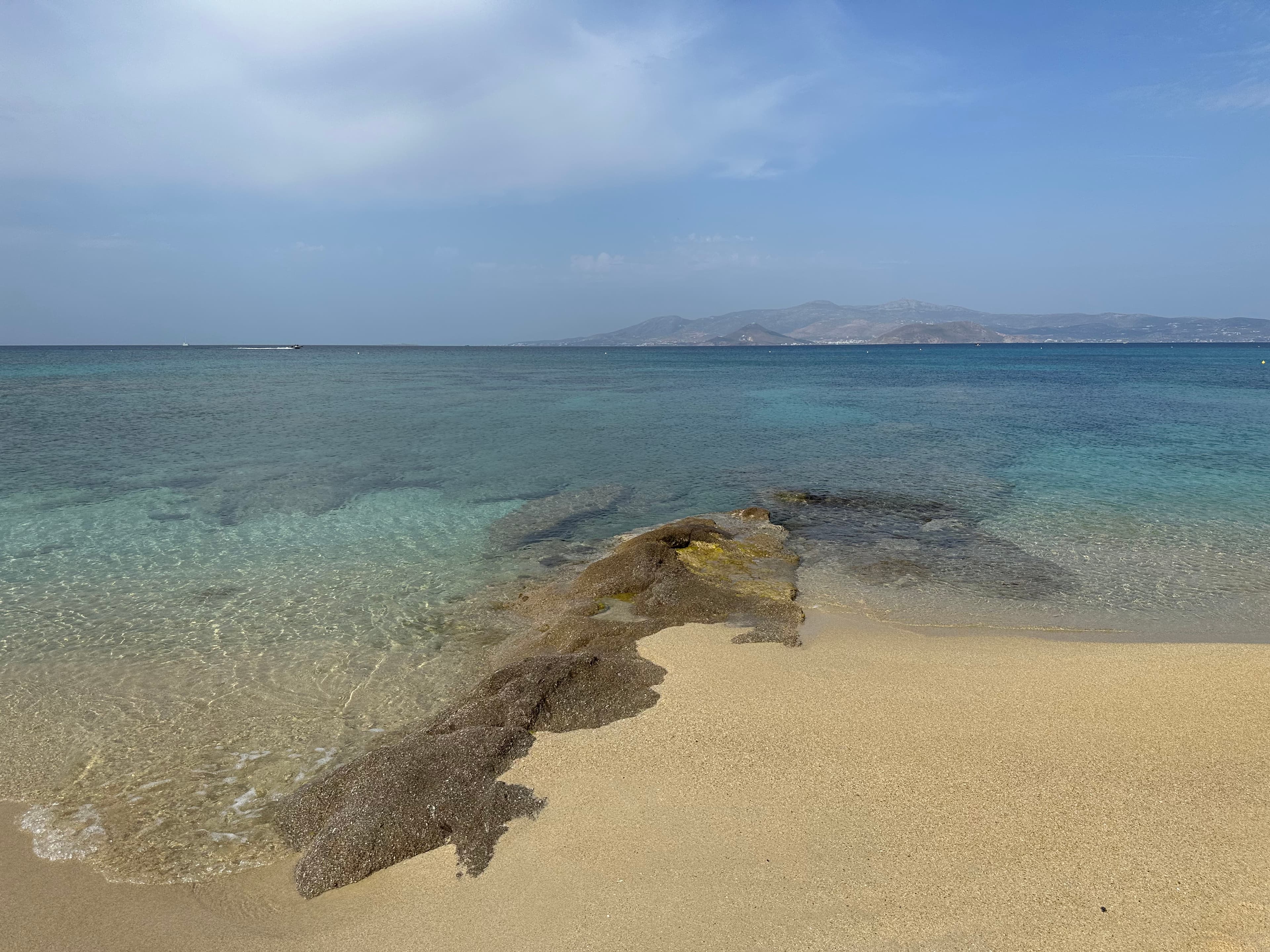 Waves lap the shore of a sandy beach on a sunny day.