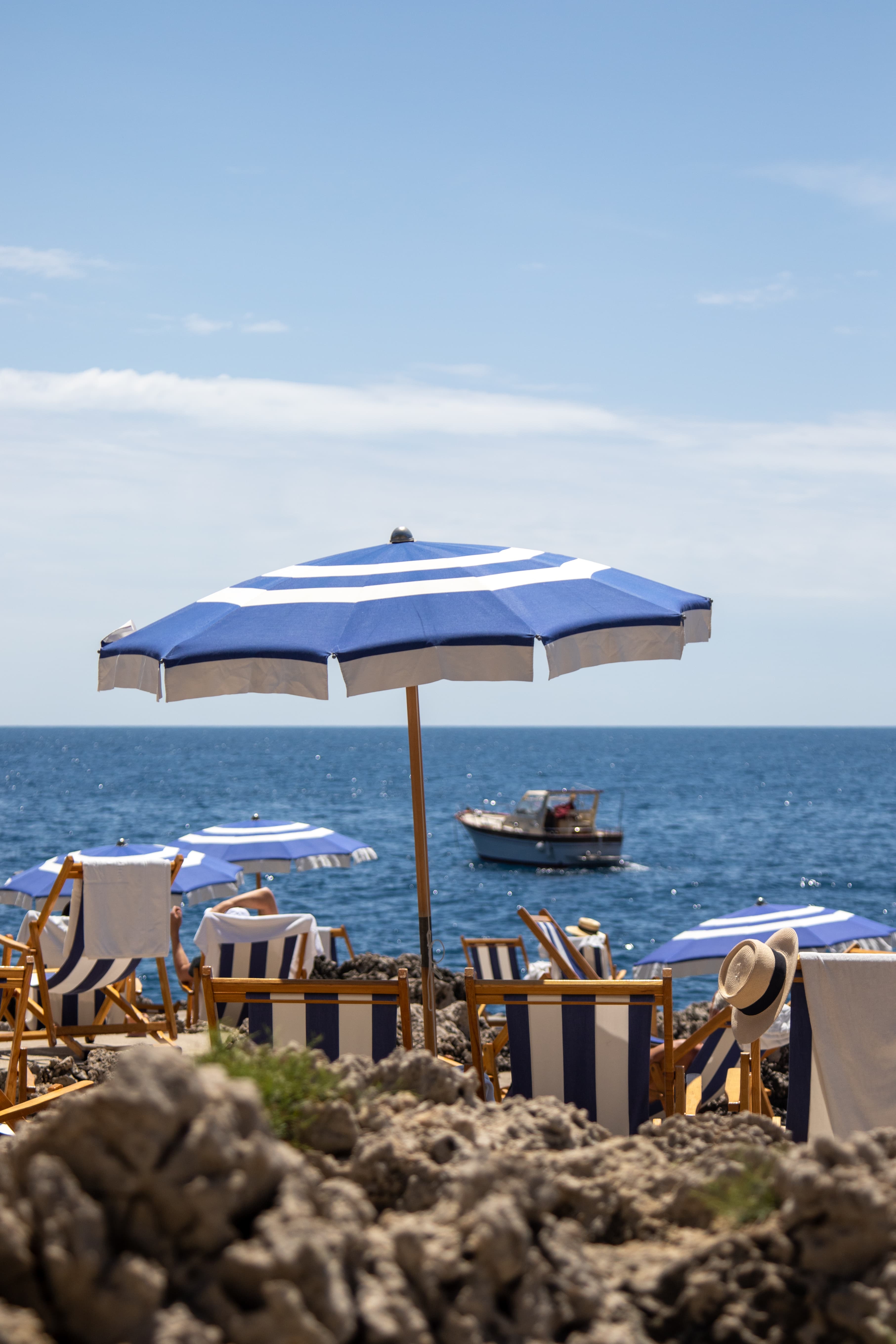 A view of a blue and white striped umbrella and lounge chairs overlooking vibrant blue waters.