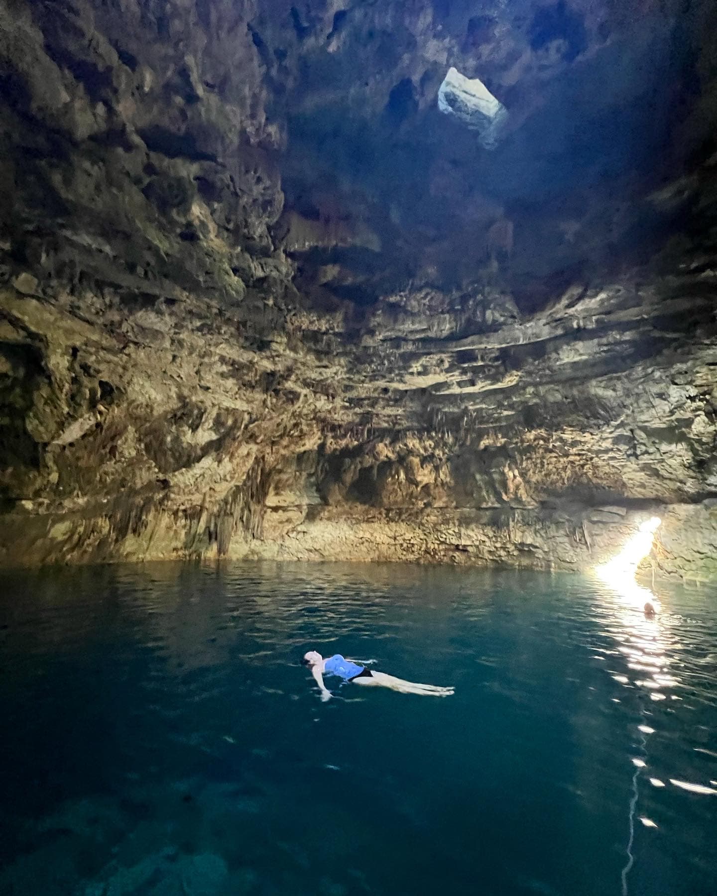 A person floating on a body of water inside of a cave.