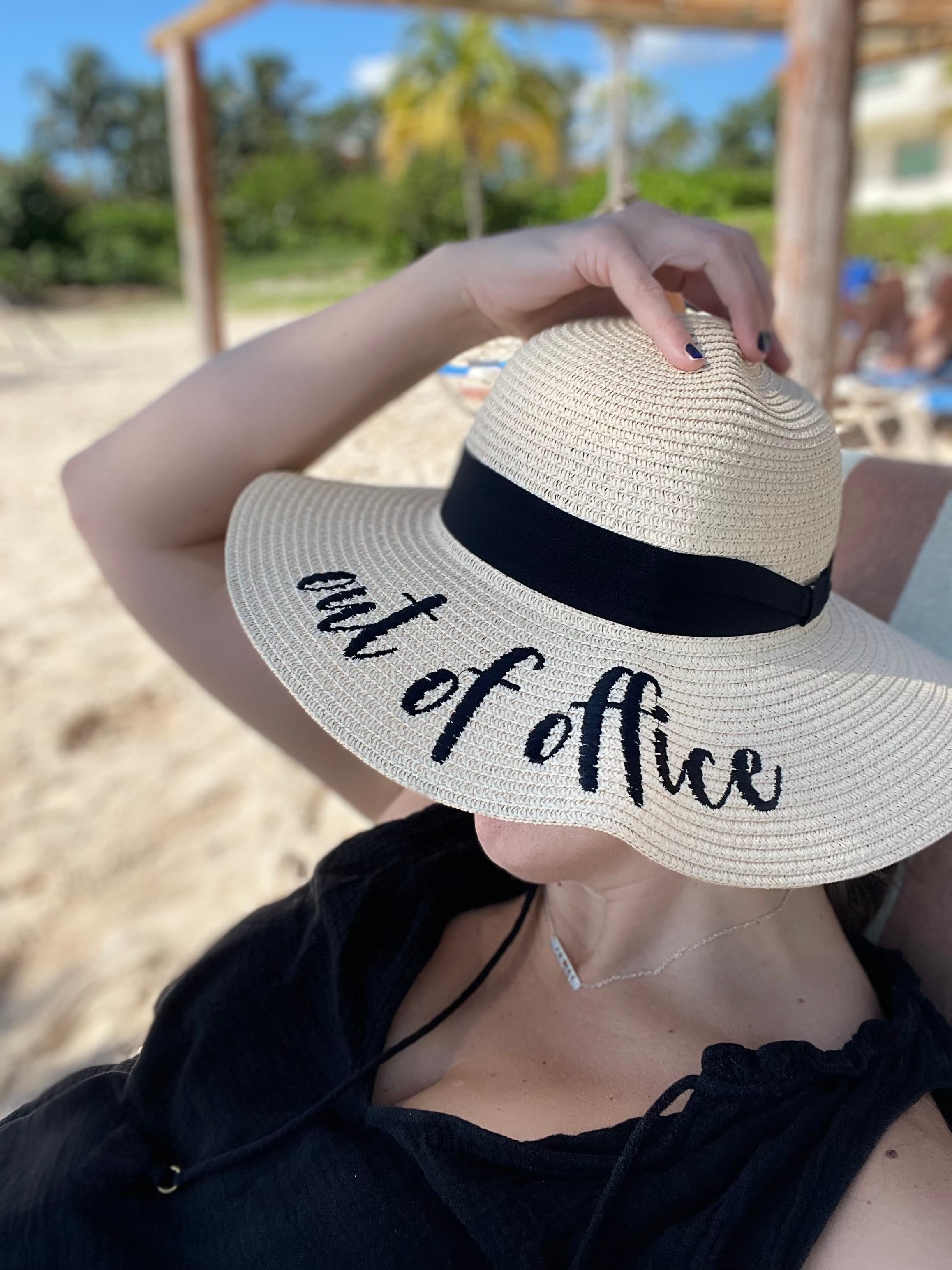 An advisor lounging on a beach and wearing a sunhat that says "out of office".