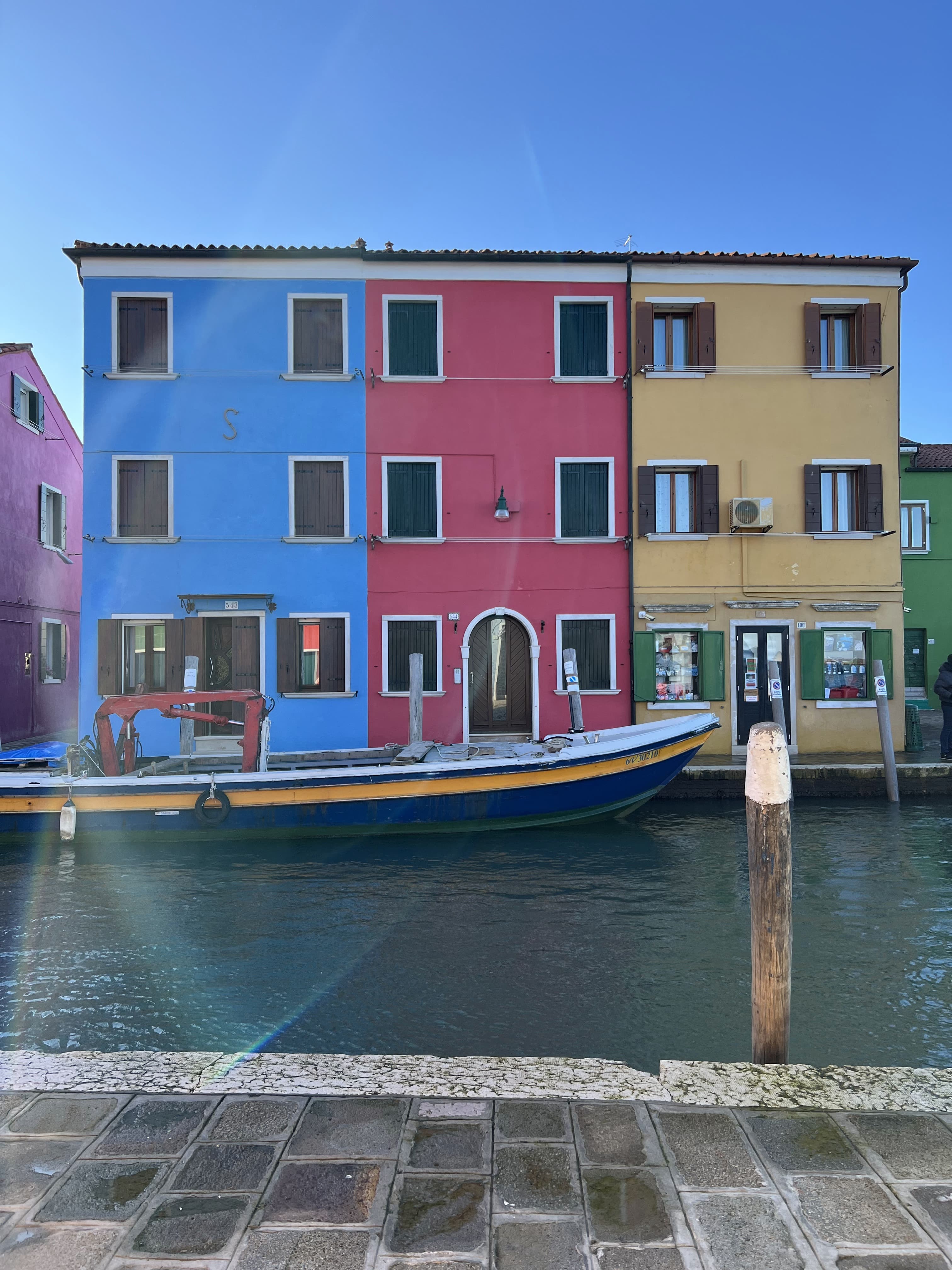 A blue, red and yellow set of homes behind a canal and boat.