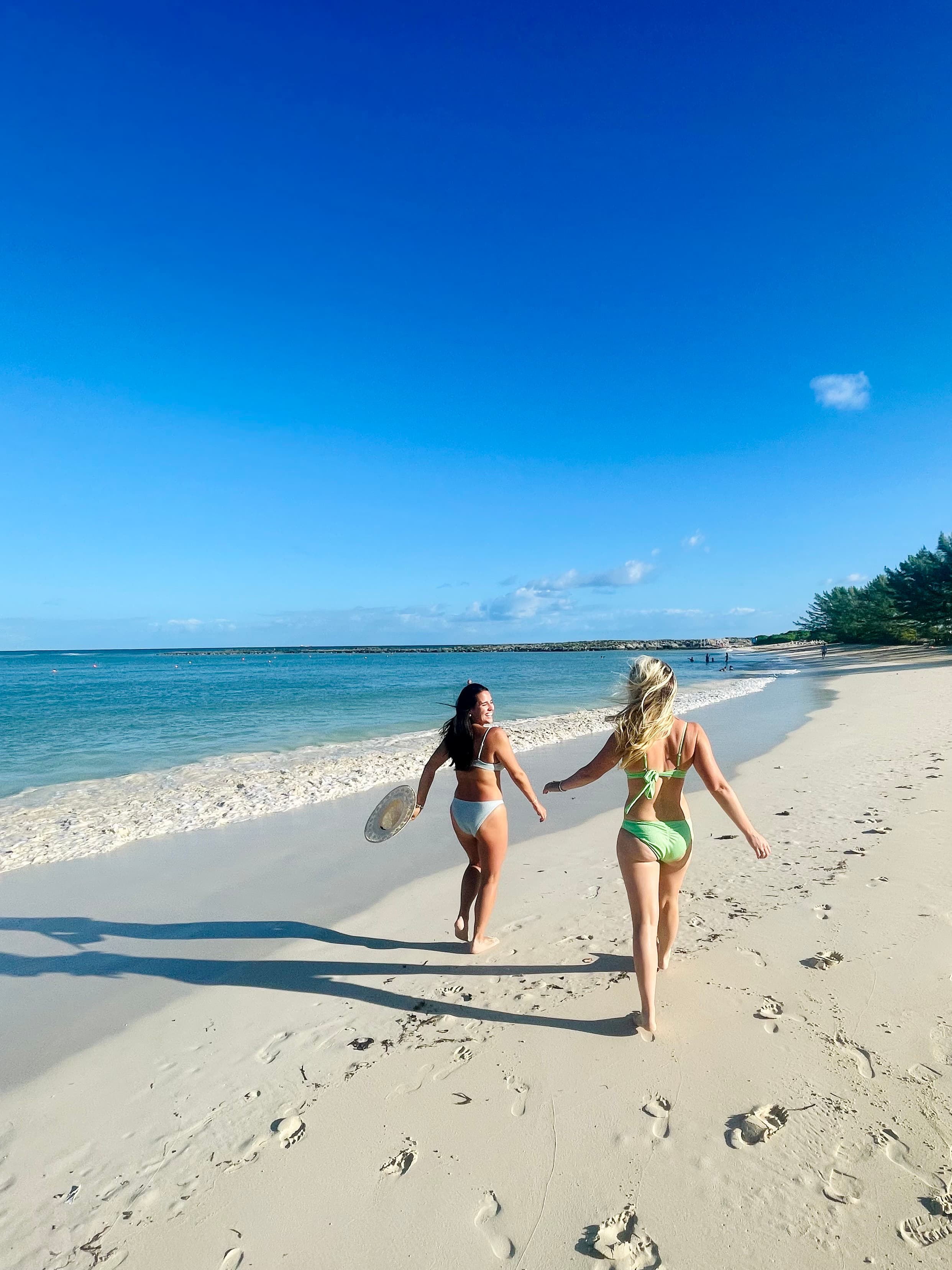 Two women in bikinis walking down a beach, away from the camera.