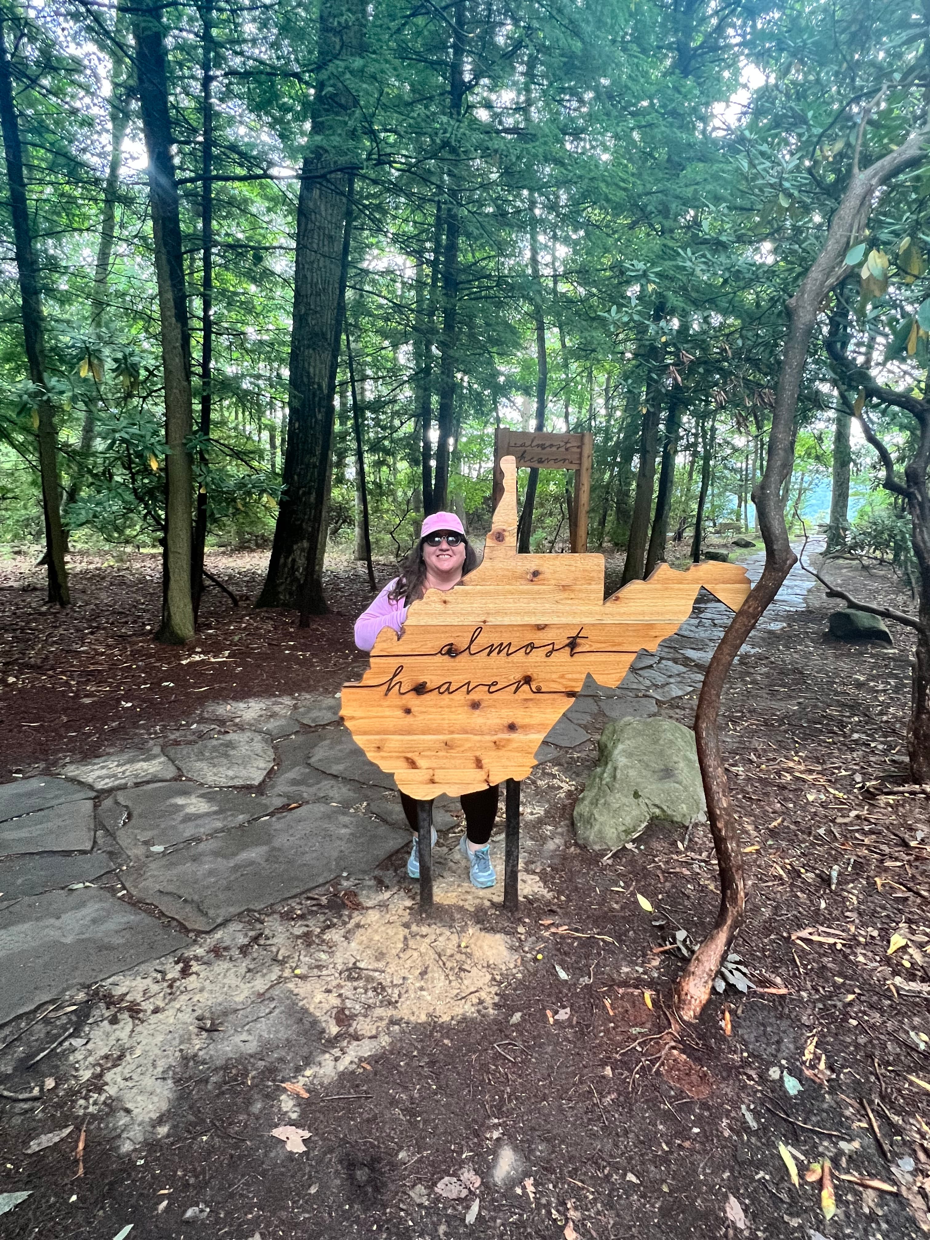 Advisor standing on a trail behind a wooden sign in the shape of West Virginia.