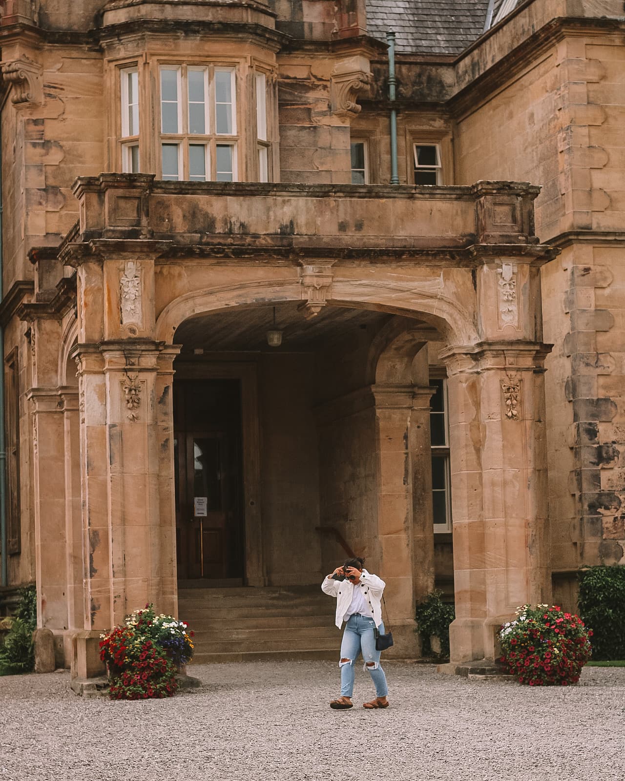 Advisor takes photo in front of large arches under a tiled roof on a sunny day.