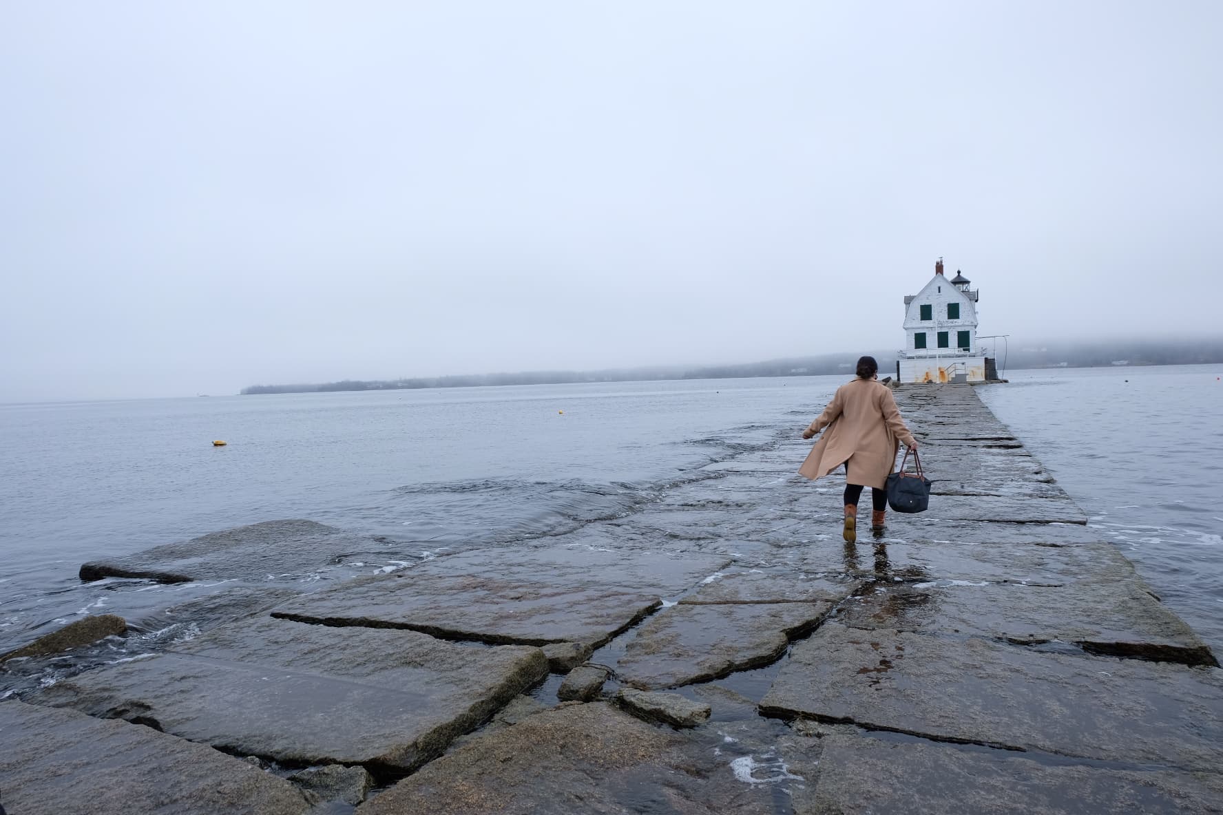 Person running in the rain over large stone steps leading to a lighthouse.