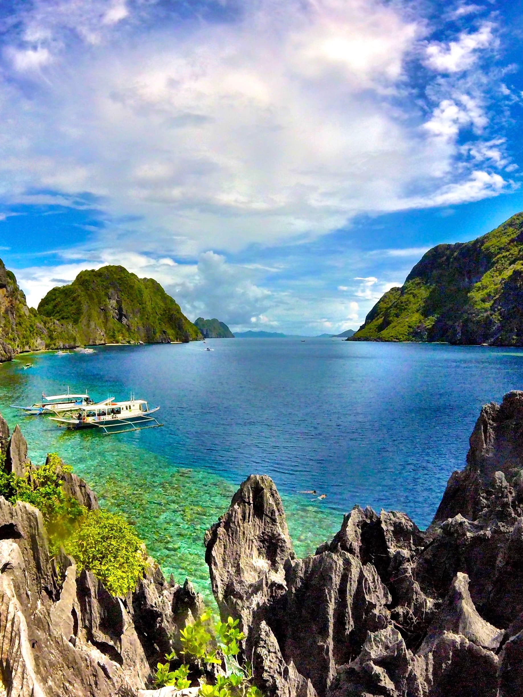 A boat lightly rocks on the gentle waves of crystal-clear water as lush island hill stretch toward the horizon on a sunny day.