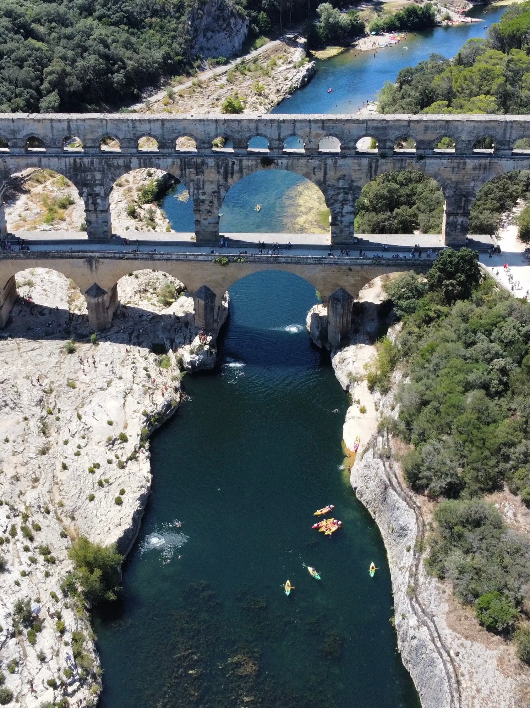 Boats wind their way through a canal as it drifts toward a bridge on a sunny day.