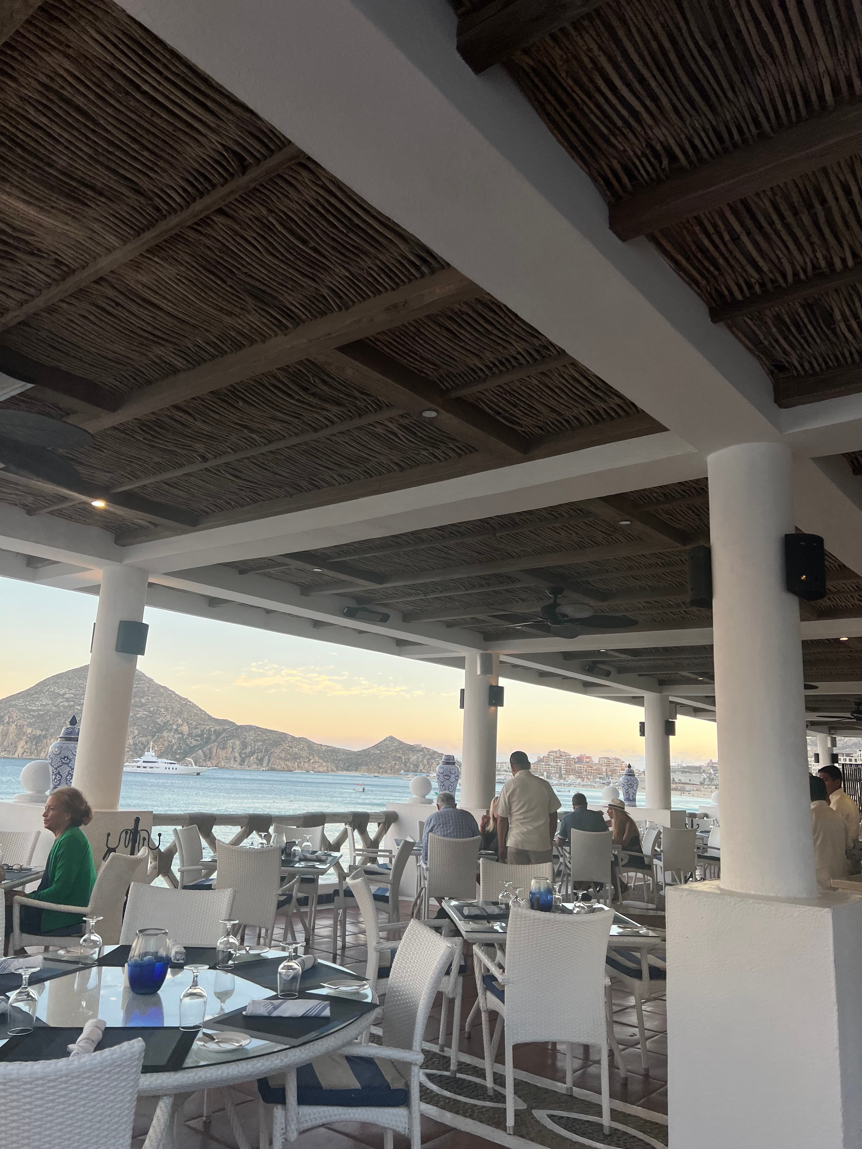 Inside of a restaurant with a view of the ocean in the background.