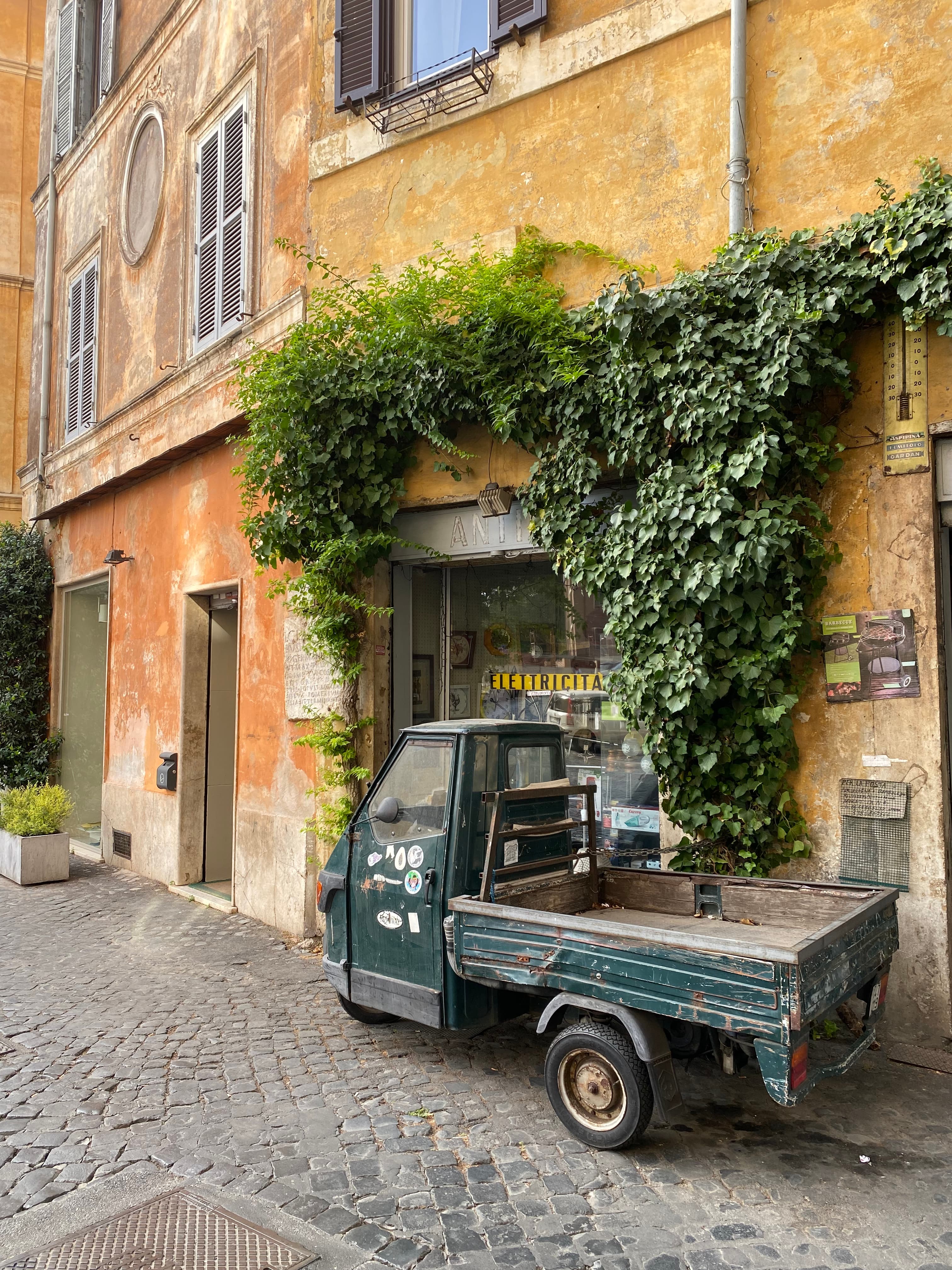 A view of a classic building with foliage and a local delivery truck in the distance