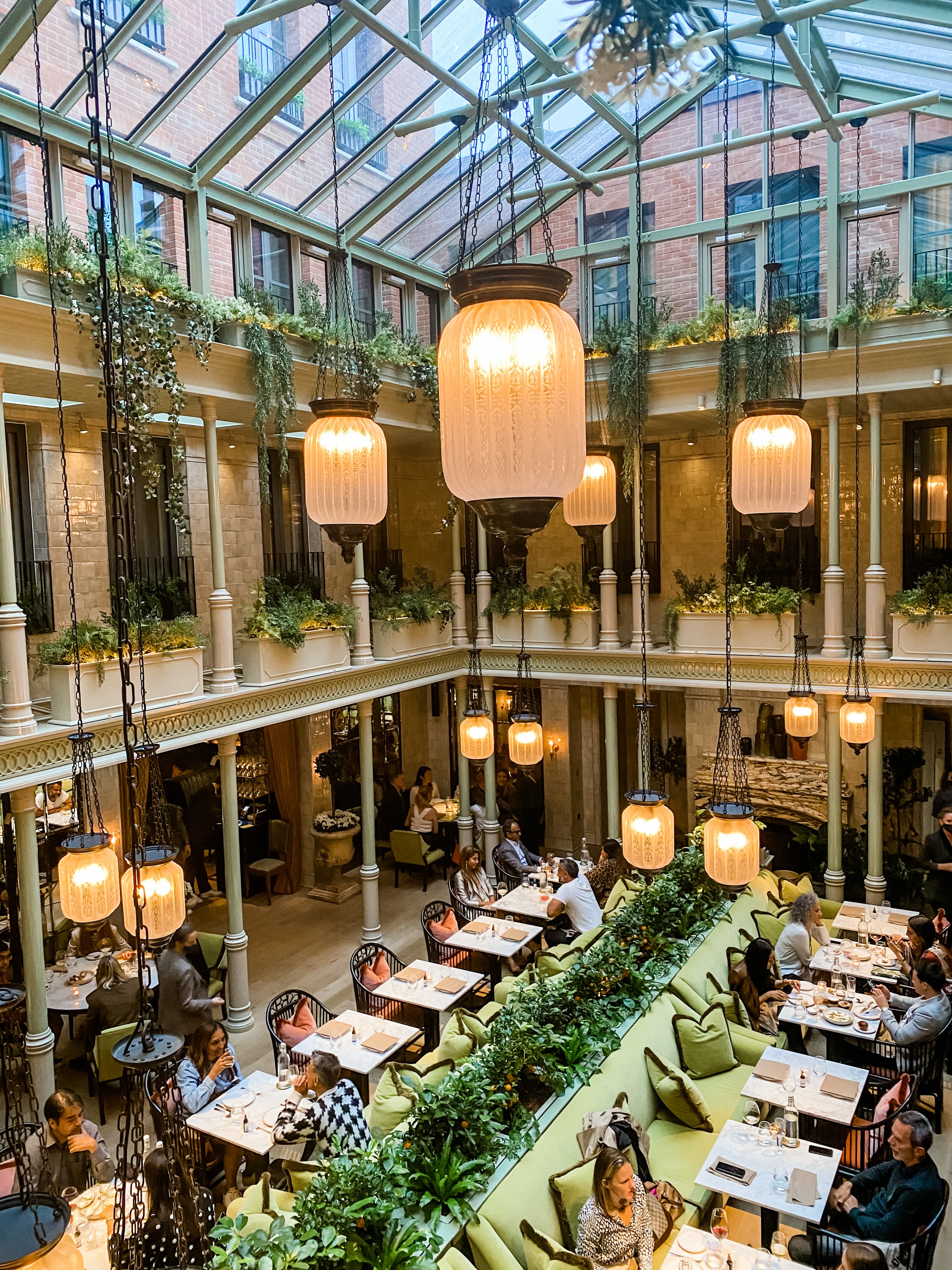 Dining tables in a hall with a glass ceiling and hanging pendant lights.