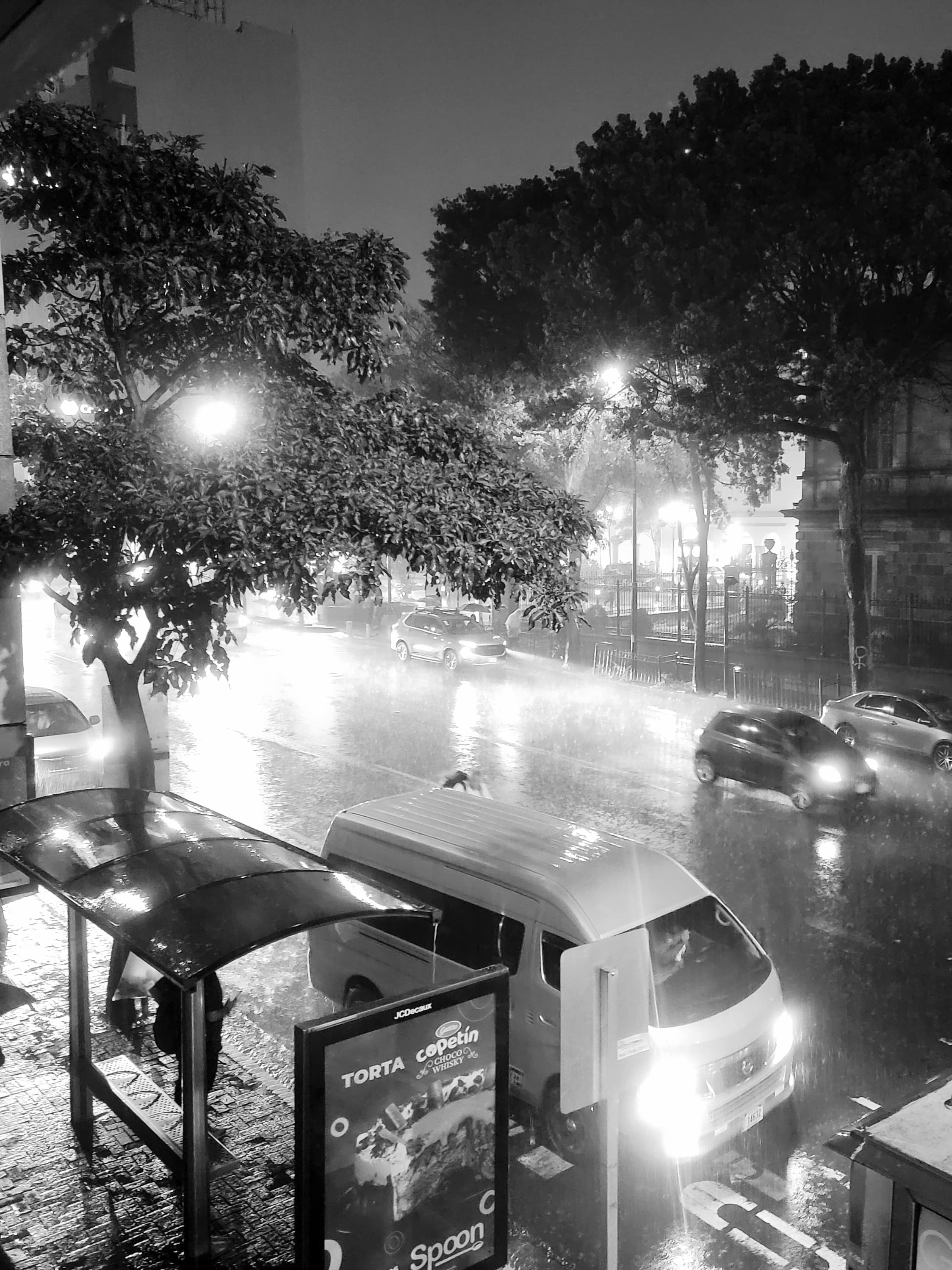Black and white photo of the city with cars driving by.