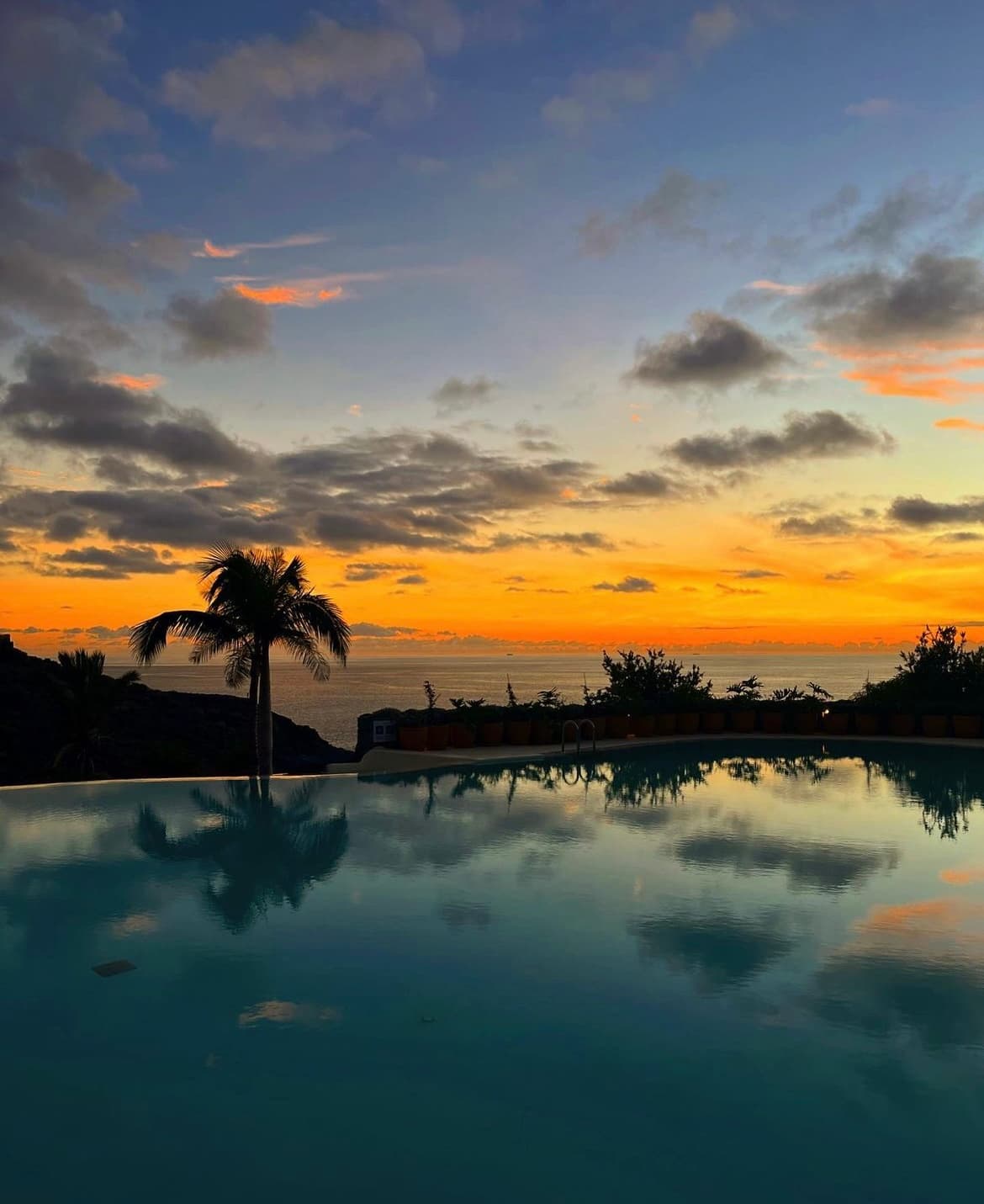 A sun setting over a pool with silhouetted palm trees in the distance.
