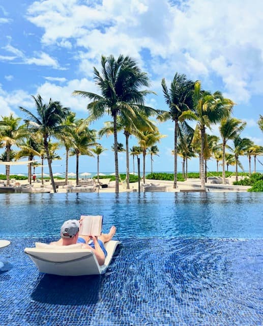 Advisor lounging in a chair in the pool with palm trees in the distance.