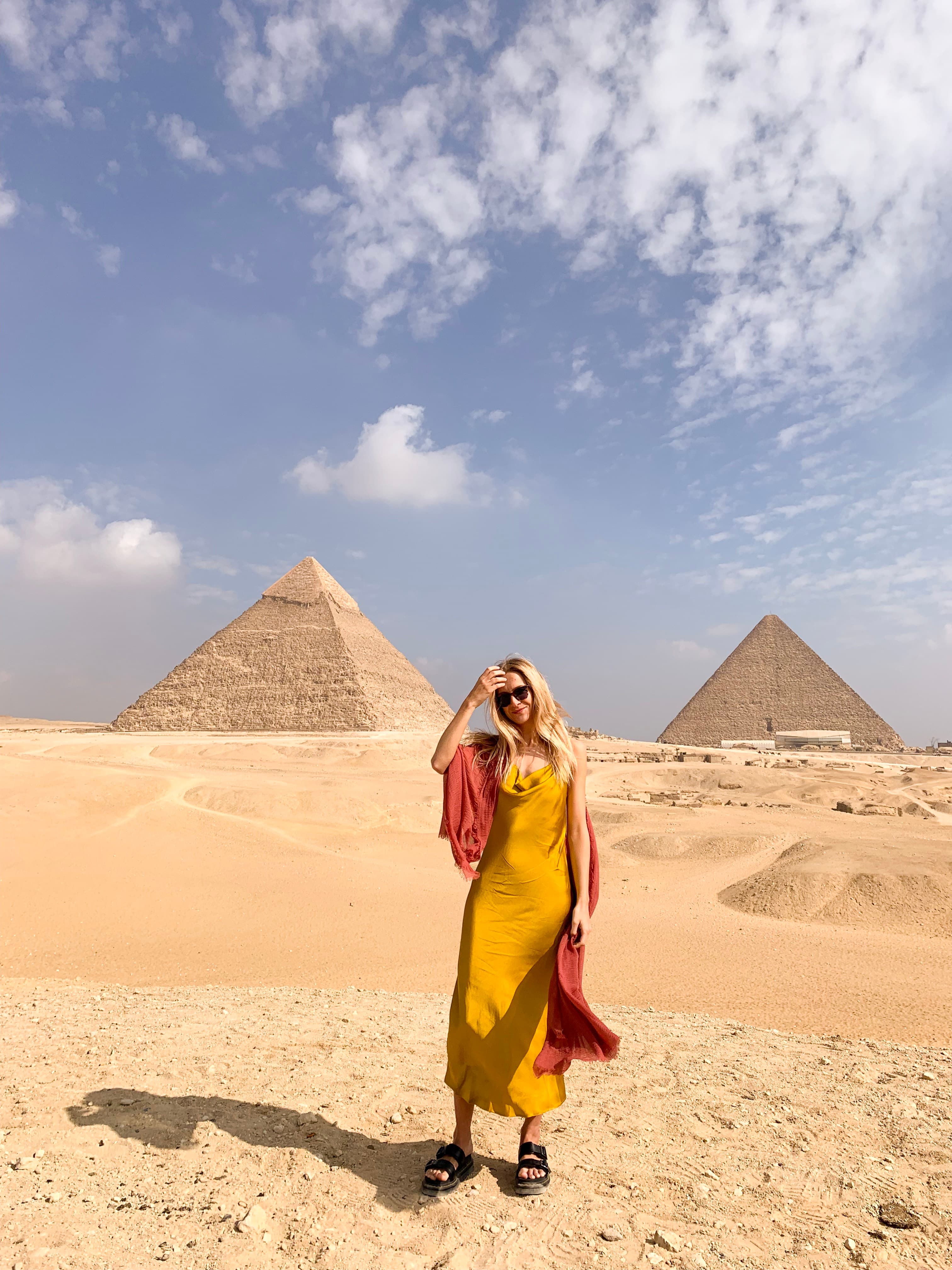 Nicola posing in a yellow dress in the desert with pyramids in the background.