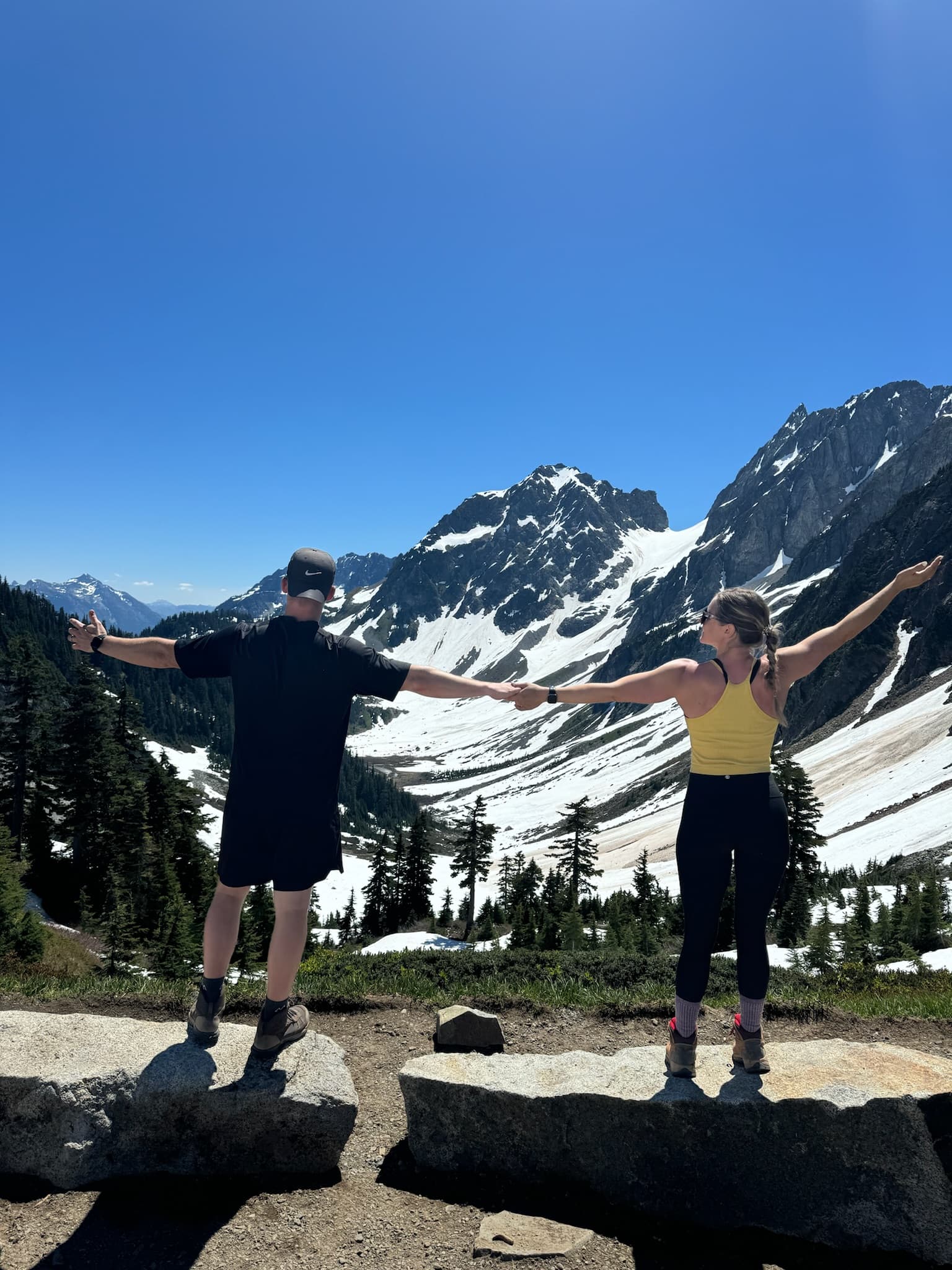 Advisor posing in front of snow-covered mountain tops in the distance on a sunny day.