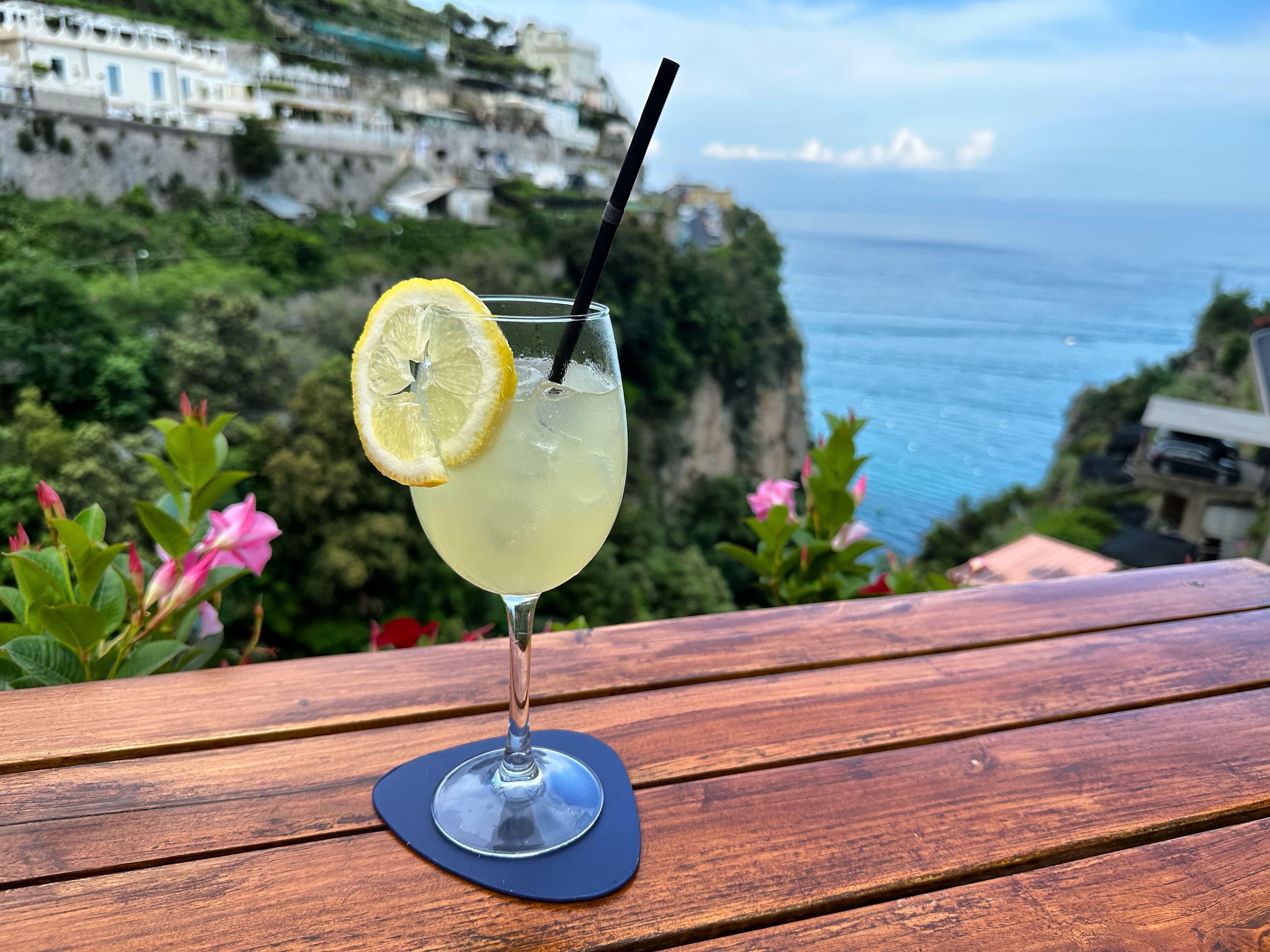 A cocktail sitting on a ledge with a body of water in the distance on a sunny day.