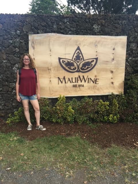 A woman posing in front of a sign outside that reads "Maui Wine."