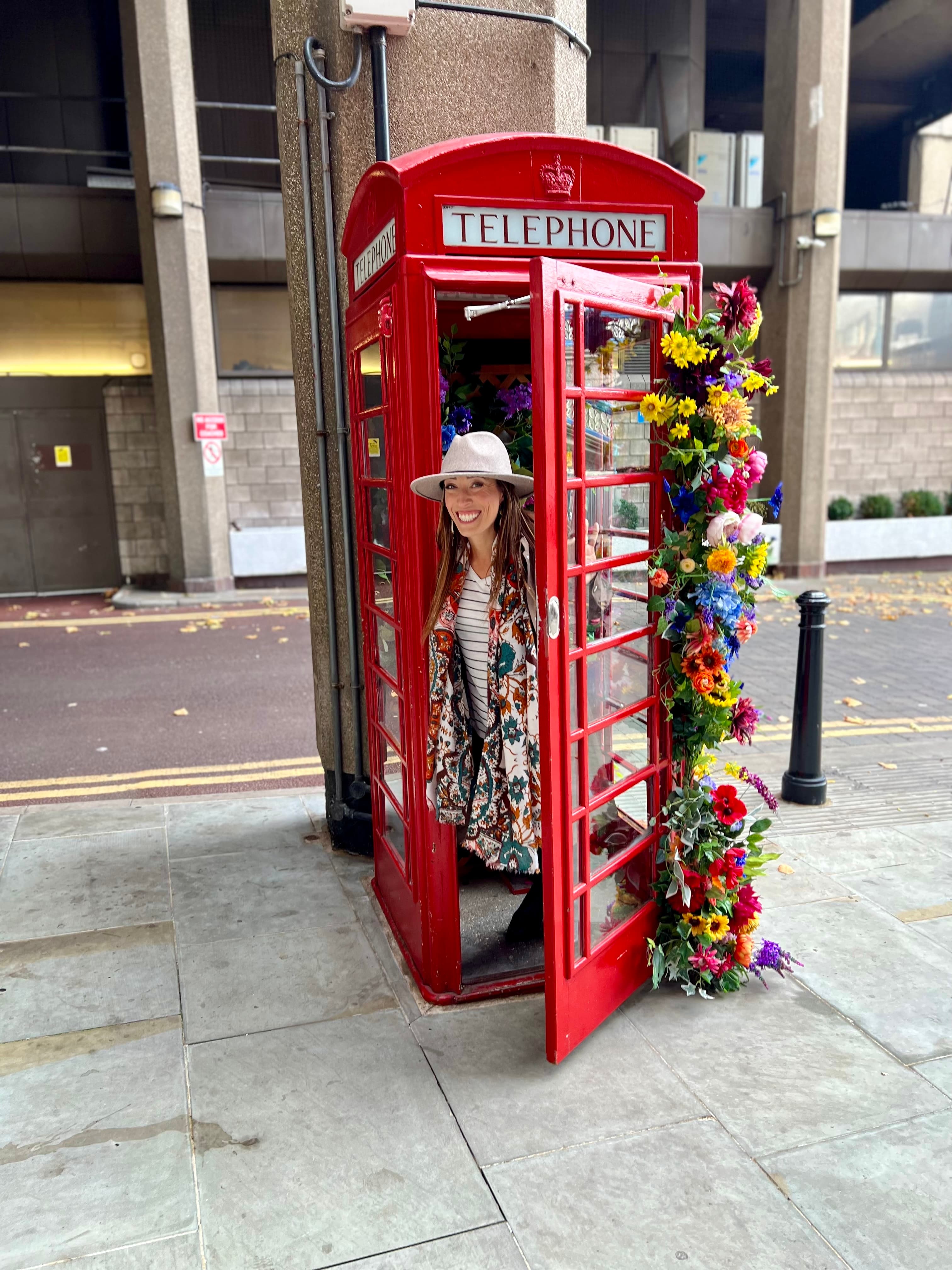 A woman smiling and posing in a red telephone booth in London, England.