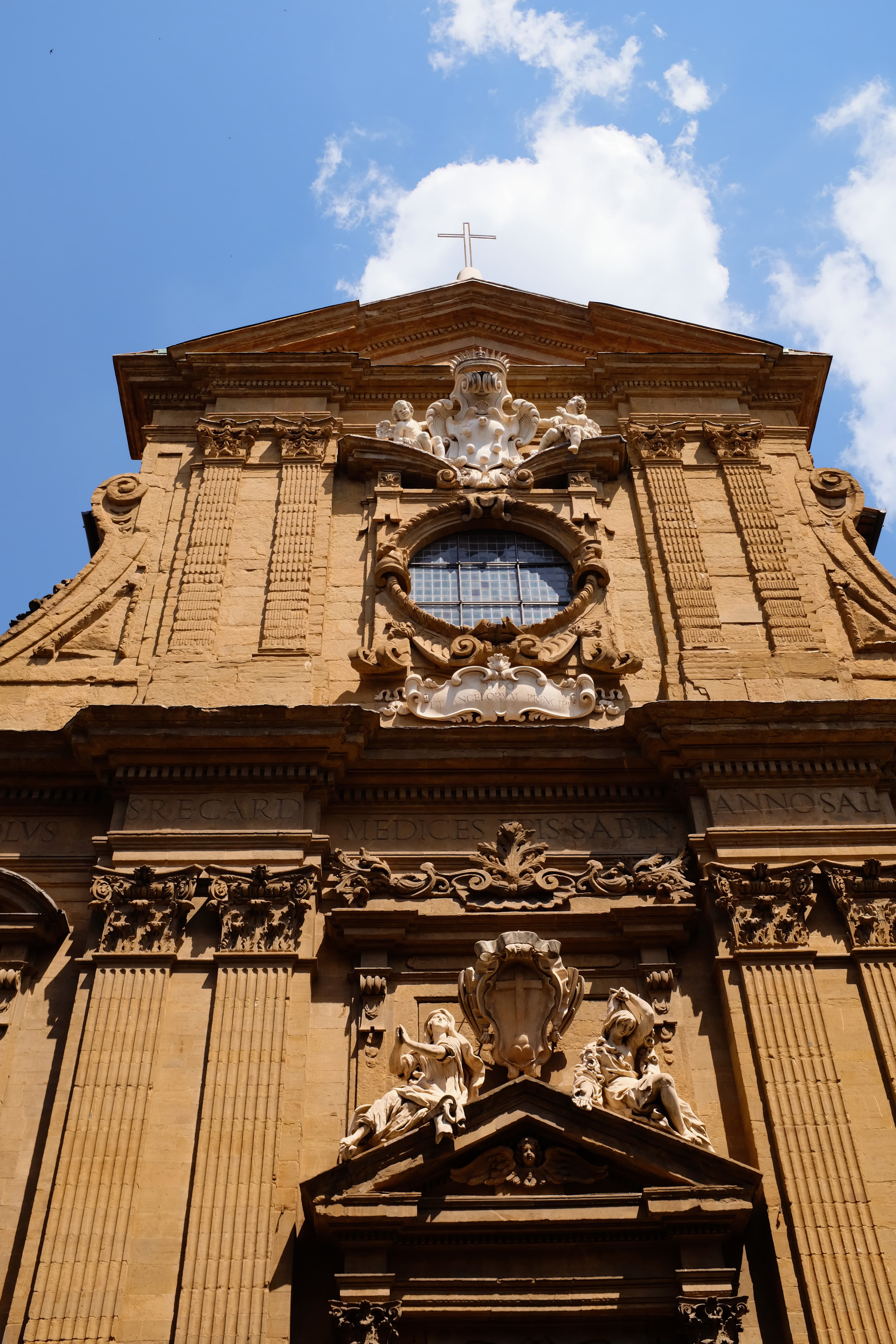 The view of a historic building with a rose window at its center on a sunny day.
