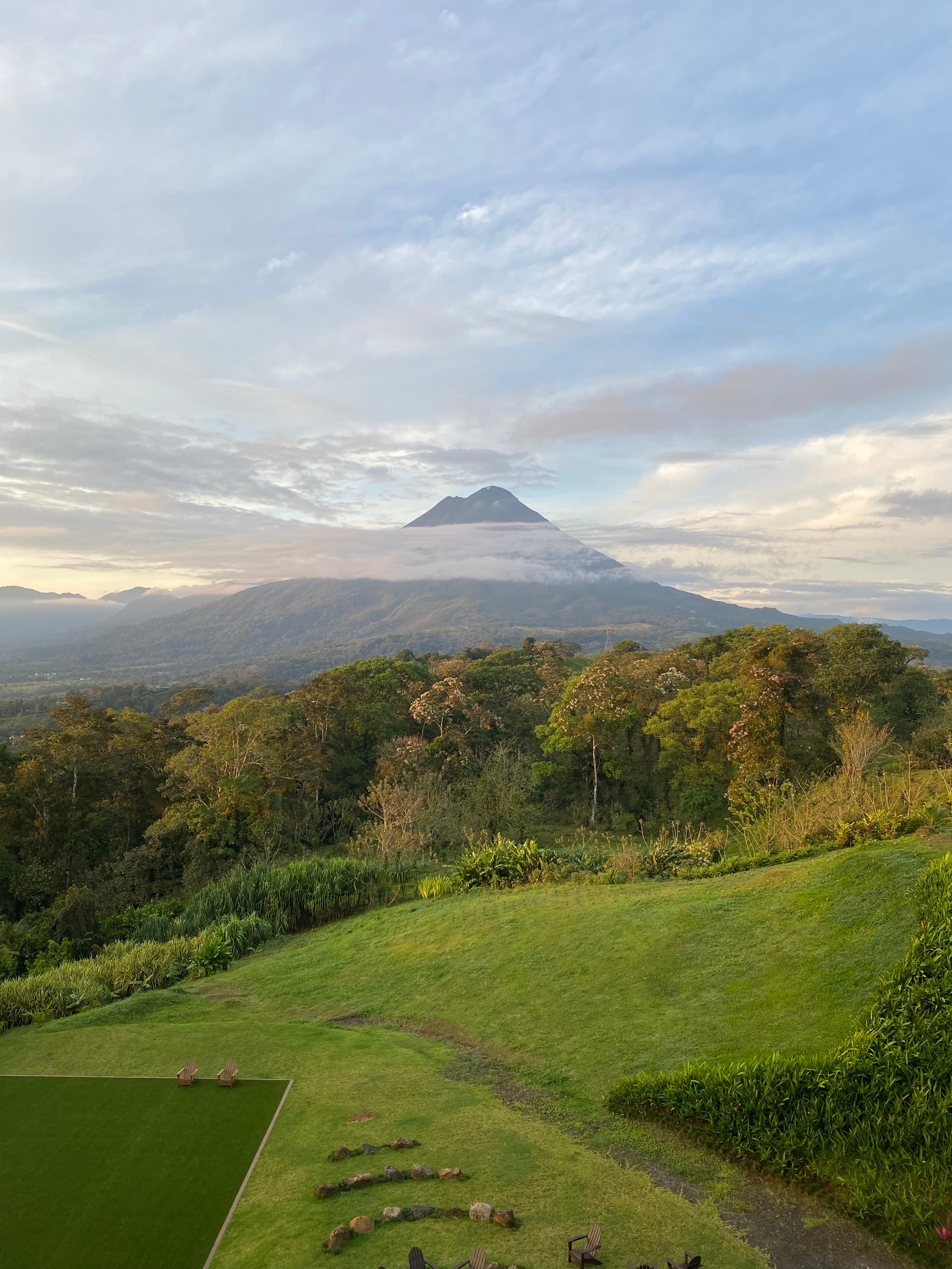 A volcano in the distance with green fields and thick jungle in the foreground.