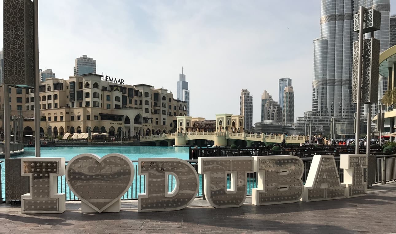 The sign welcoming you to Dubai on a sunny day near the water's edge.
