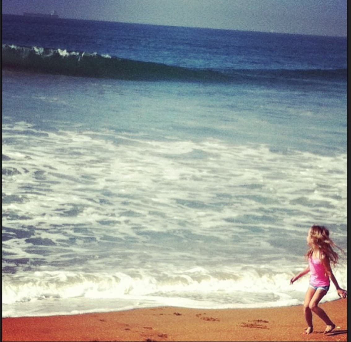A view of the beach with a child enjoying the beach and a sunny day.