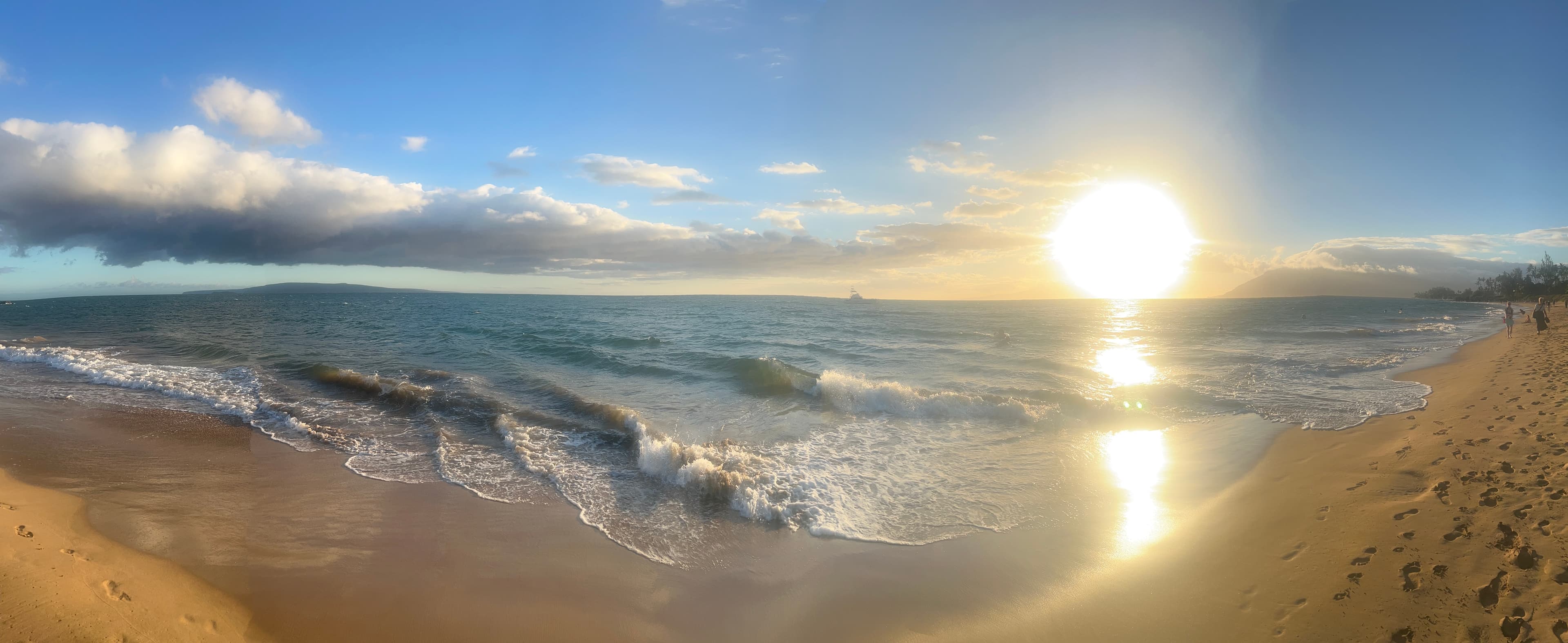 The sun begins to set on the horizon as waves gently lap the sandy shore.