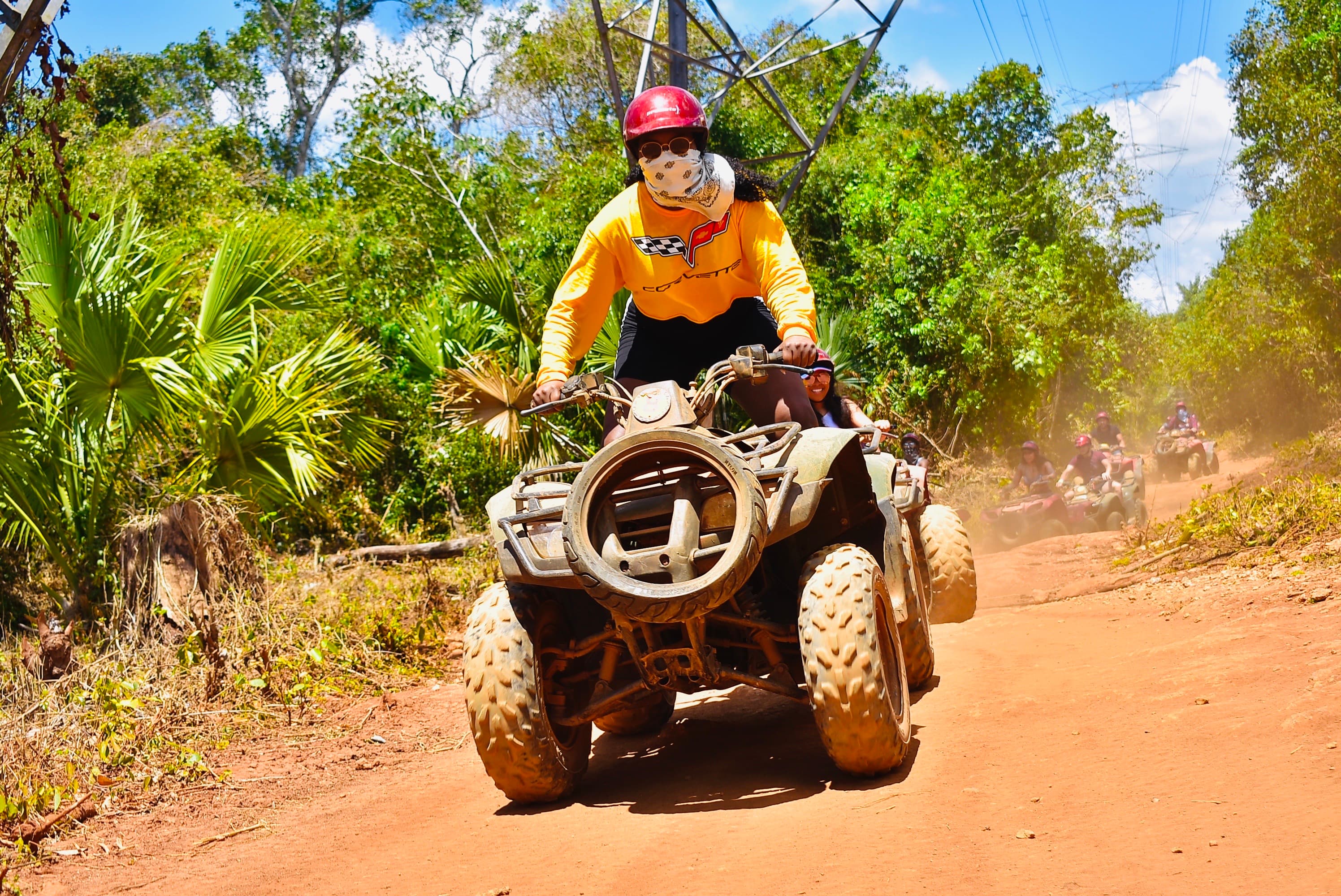 Advisor driving an ATV in a tropical region with a dirt road on a sunny day.