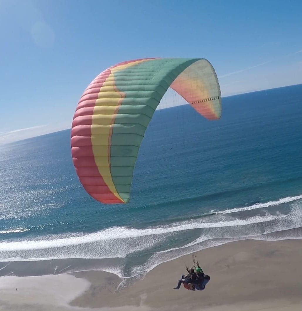 Overhead view of people parasailing above a beautiful wide beach on a sunny day